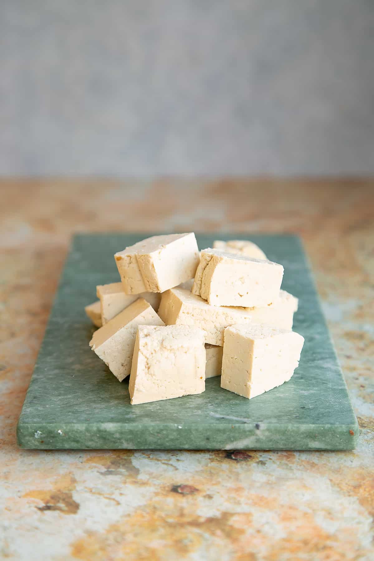 extra firm tofu cut into slices on. a green marble cutting board.