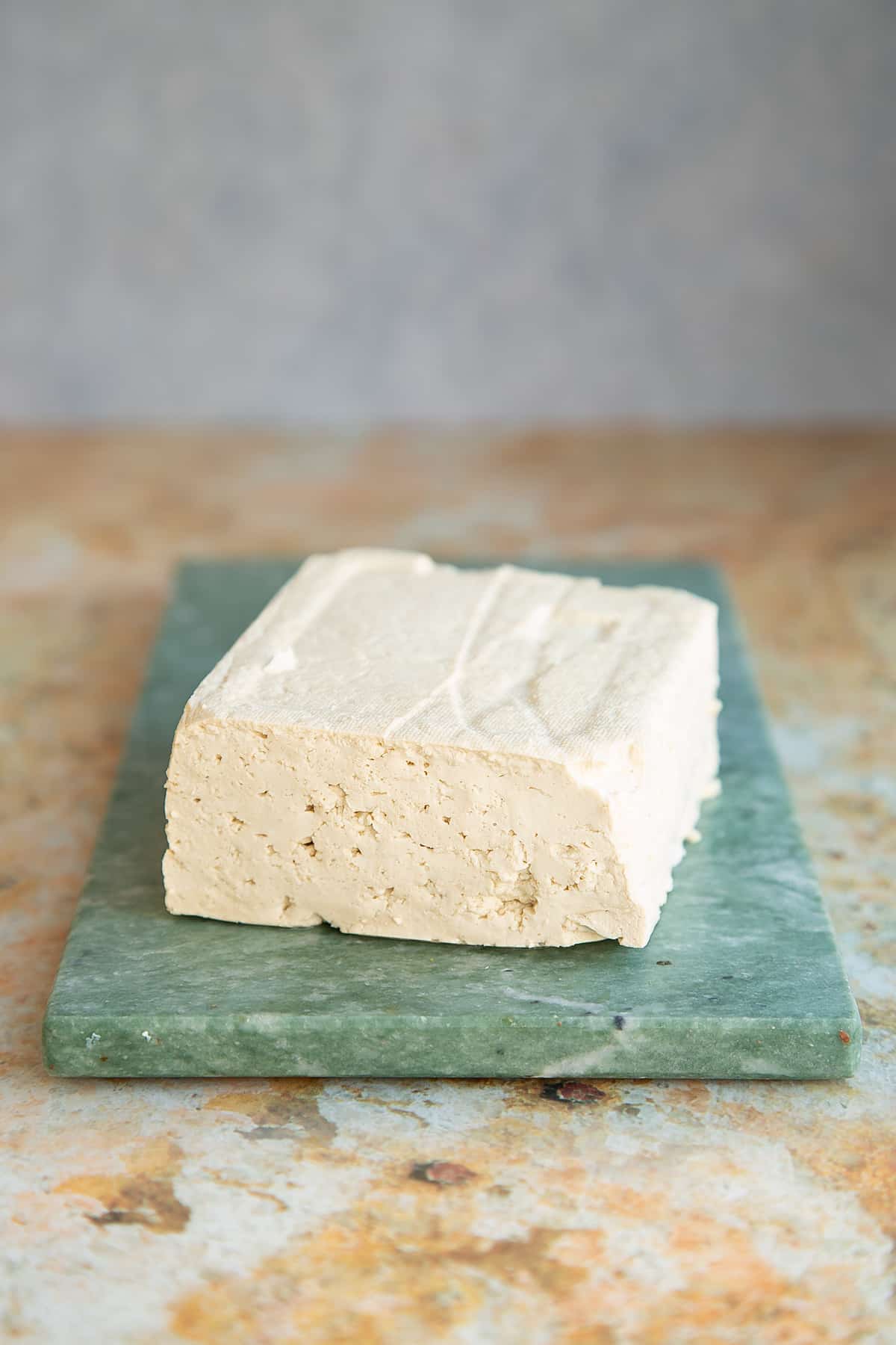 a block of firm tofu on a green marble chopping board.