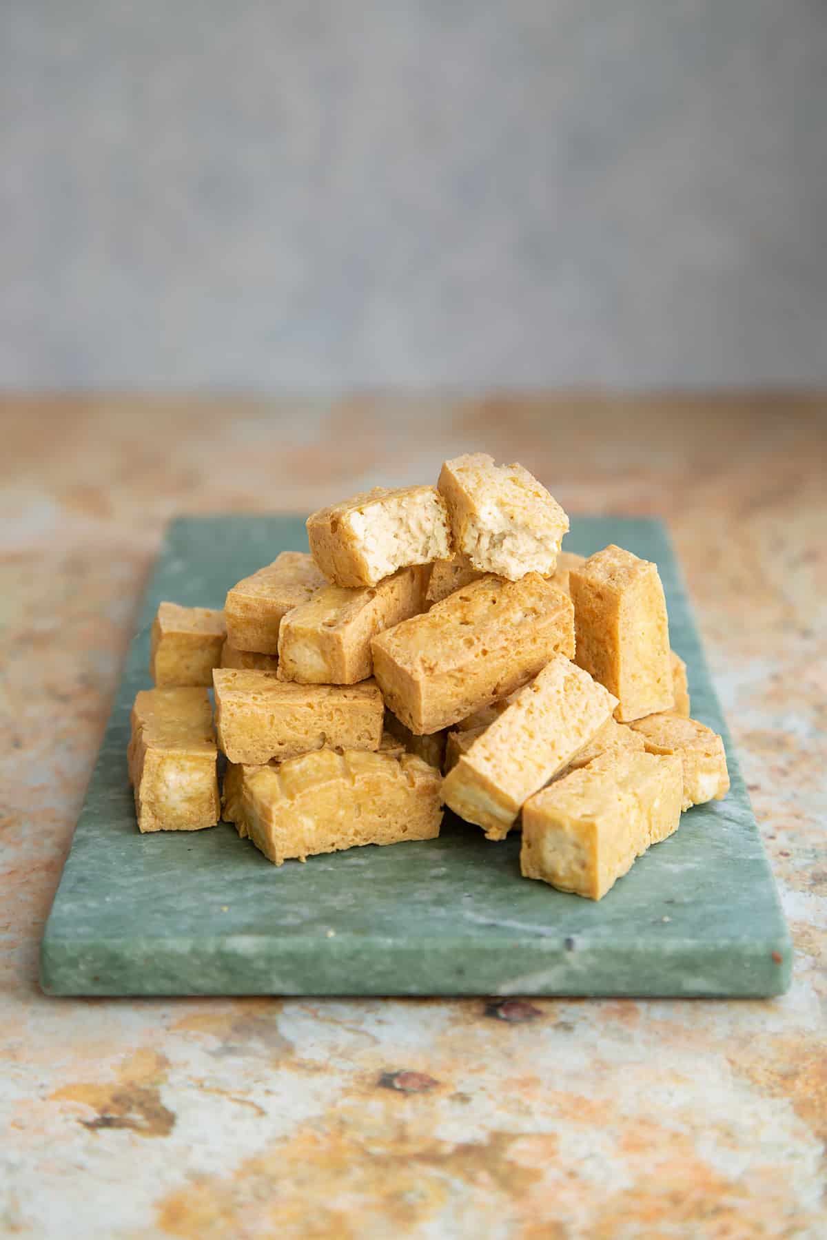 marinated pressed tofu chopped into cubes on a green marble board.