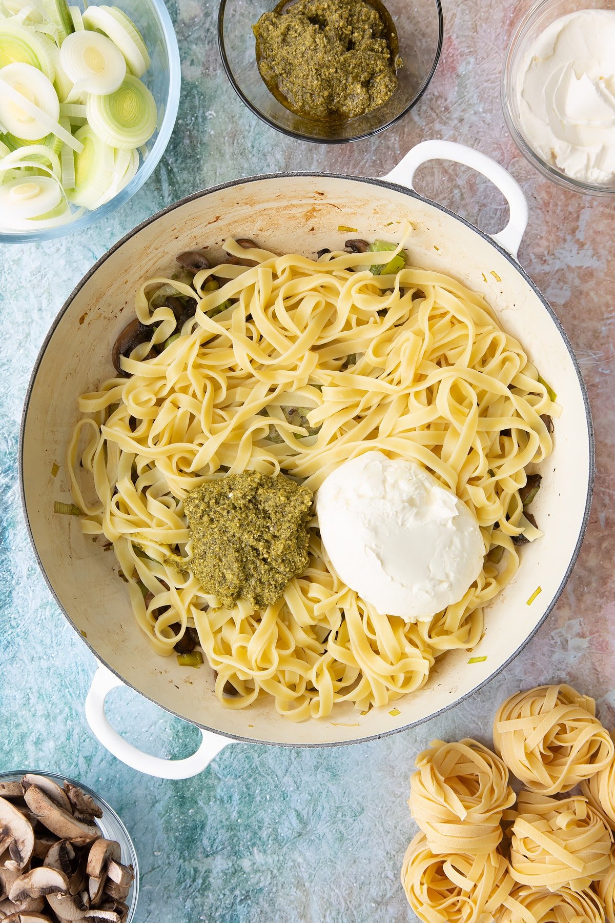 Adding pasta, crème fraîche, pesto  to the pan.