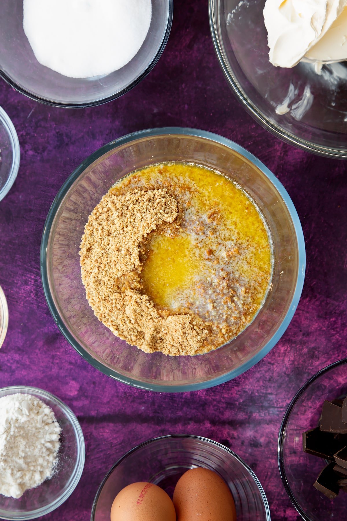 Adding the melted butter to the crumbled biscuits in a mixing bowl.