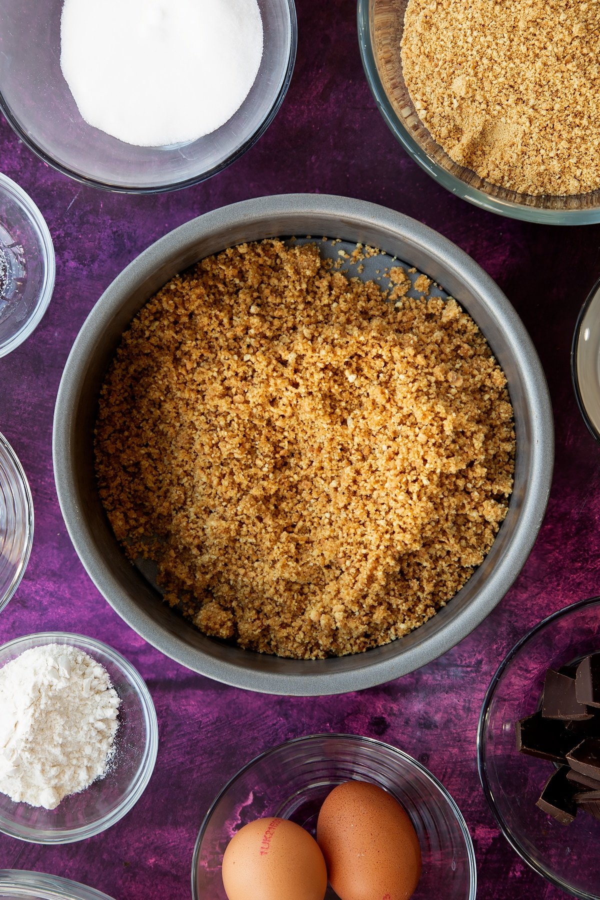 Emptying the crumbled biscuits and butter mixture into the bottom of a non-stick cake tin.