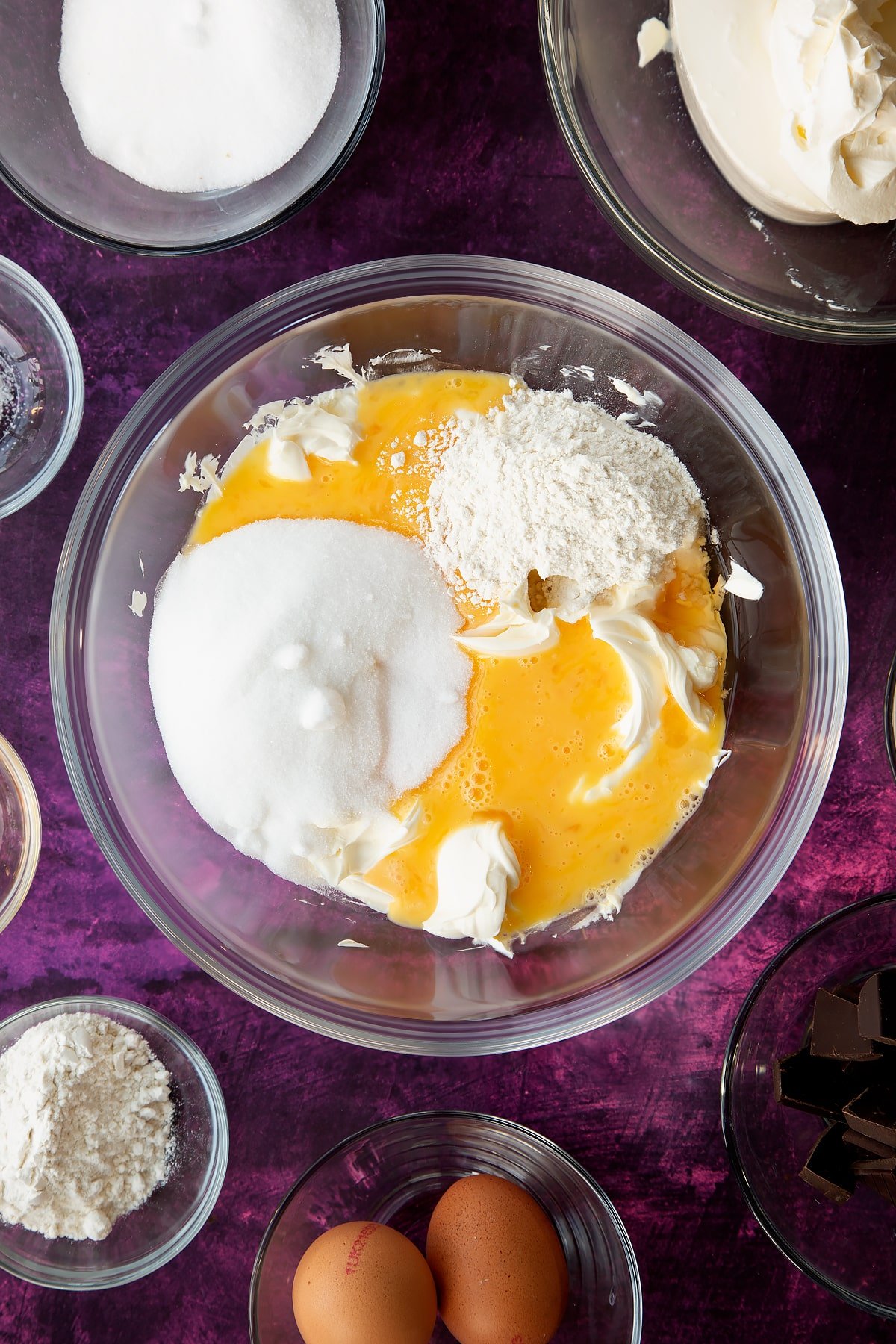 Adding eggs, sugar and flour to the cream cheese mixture in the mixing bowl.