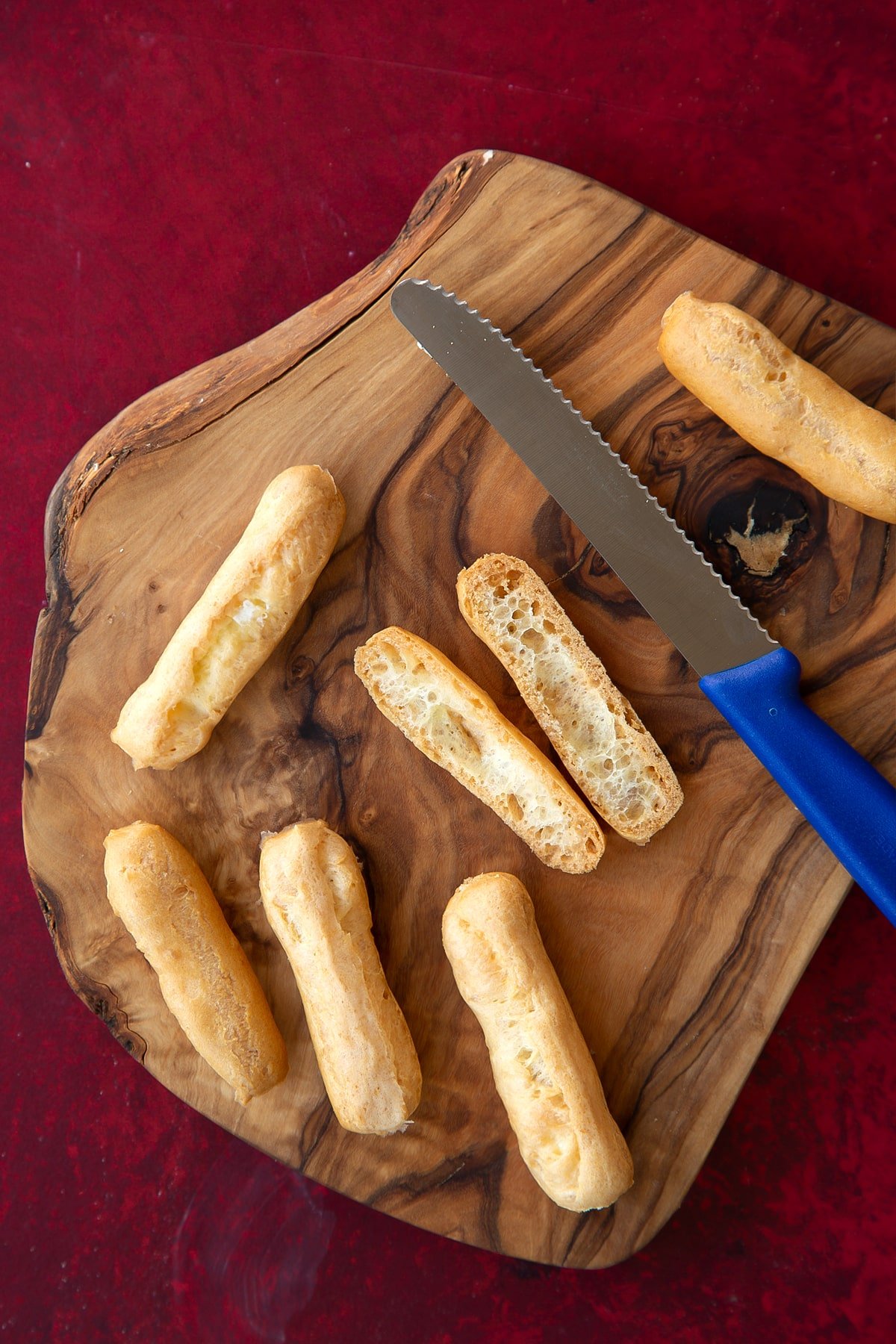 Overhead shot of the cut open mini eclairs on a wooden board with a knife on the side.