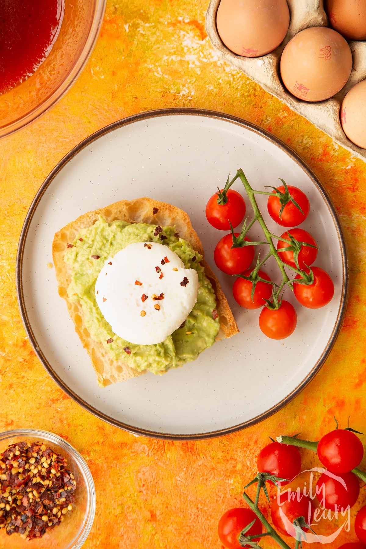 Overhead shot of avocado and toast with a poached egg on the top and a vine of tomatoes on the side.