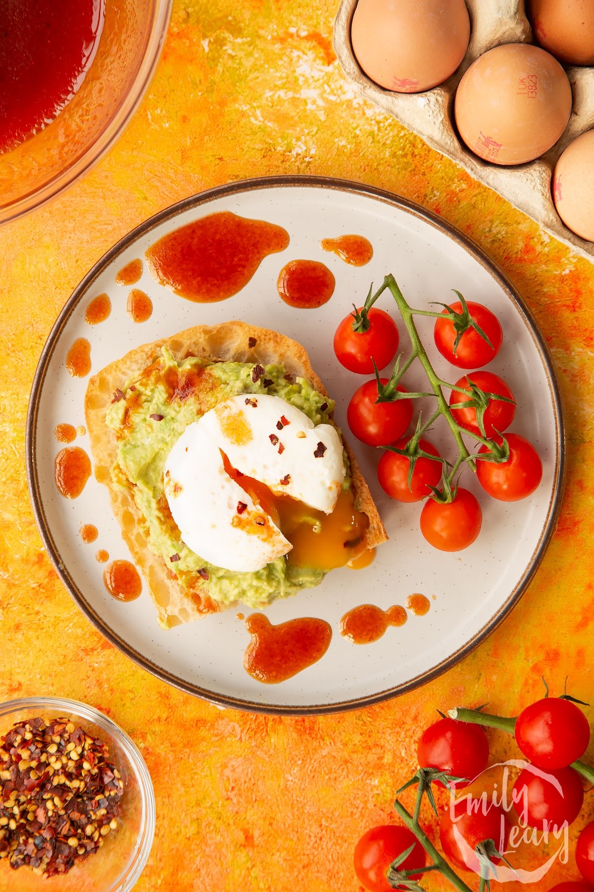 Poached egg cut open on avocado on toast with vine tomatoes on the side.