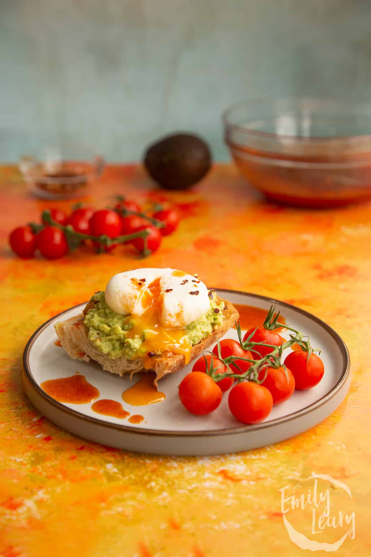 Side on shot of avocado on toast with a poached egg on the top and tomatoes on the vine on the side.