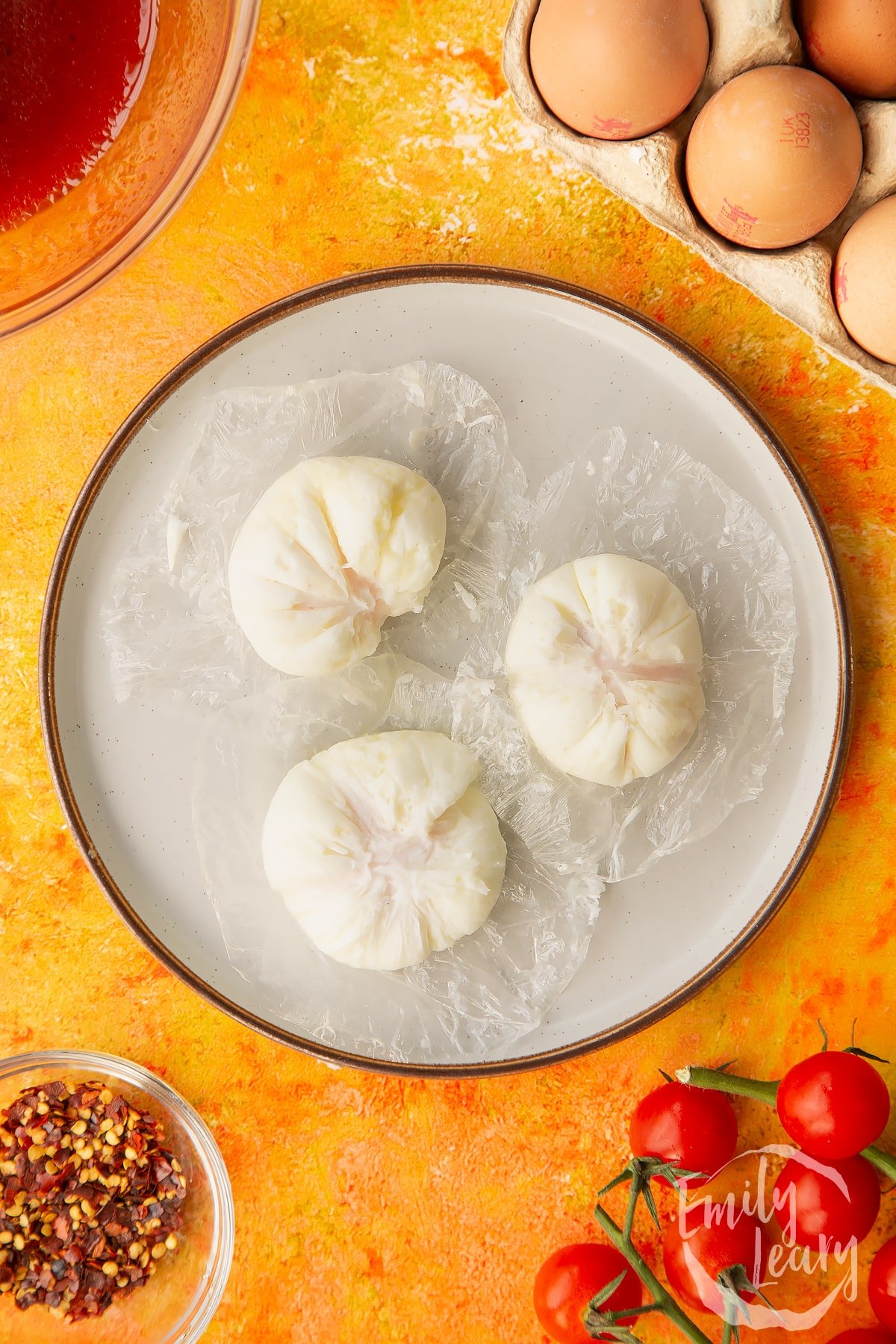 Overhead shot of three eggs being unwrapped from their clingfilm on a decorative plate.