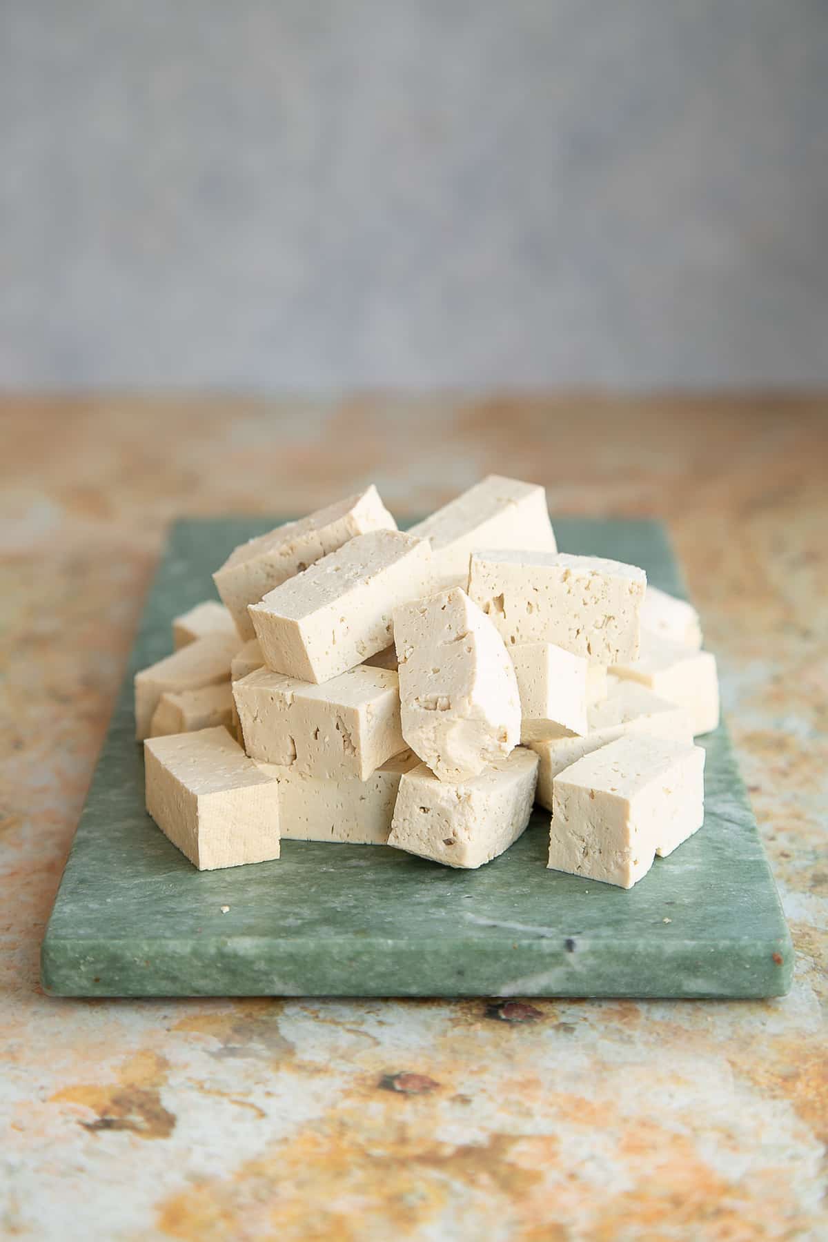 pressed firm tofu chopped into squares and cubes on a green marble vboard.