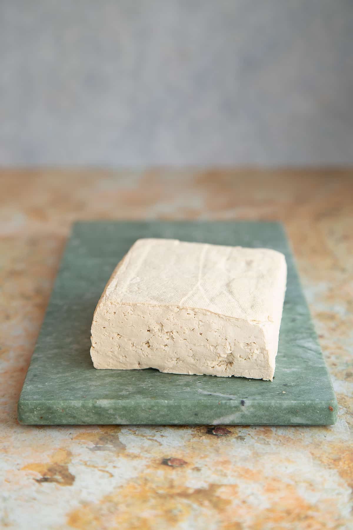 a block of extra firm tofu on a green marble board.