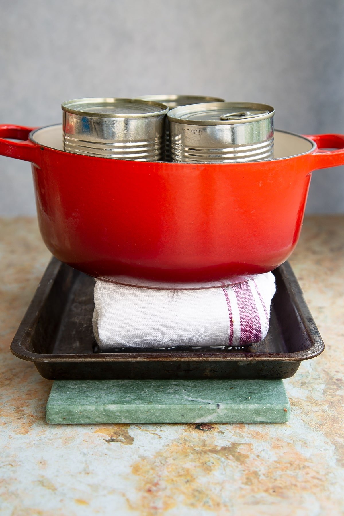 a large red pan with 3 sealed cans in the middle sat on a teatowel and bakind tray