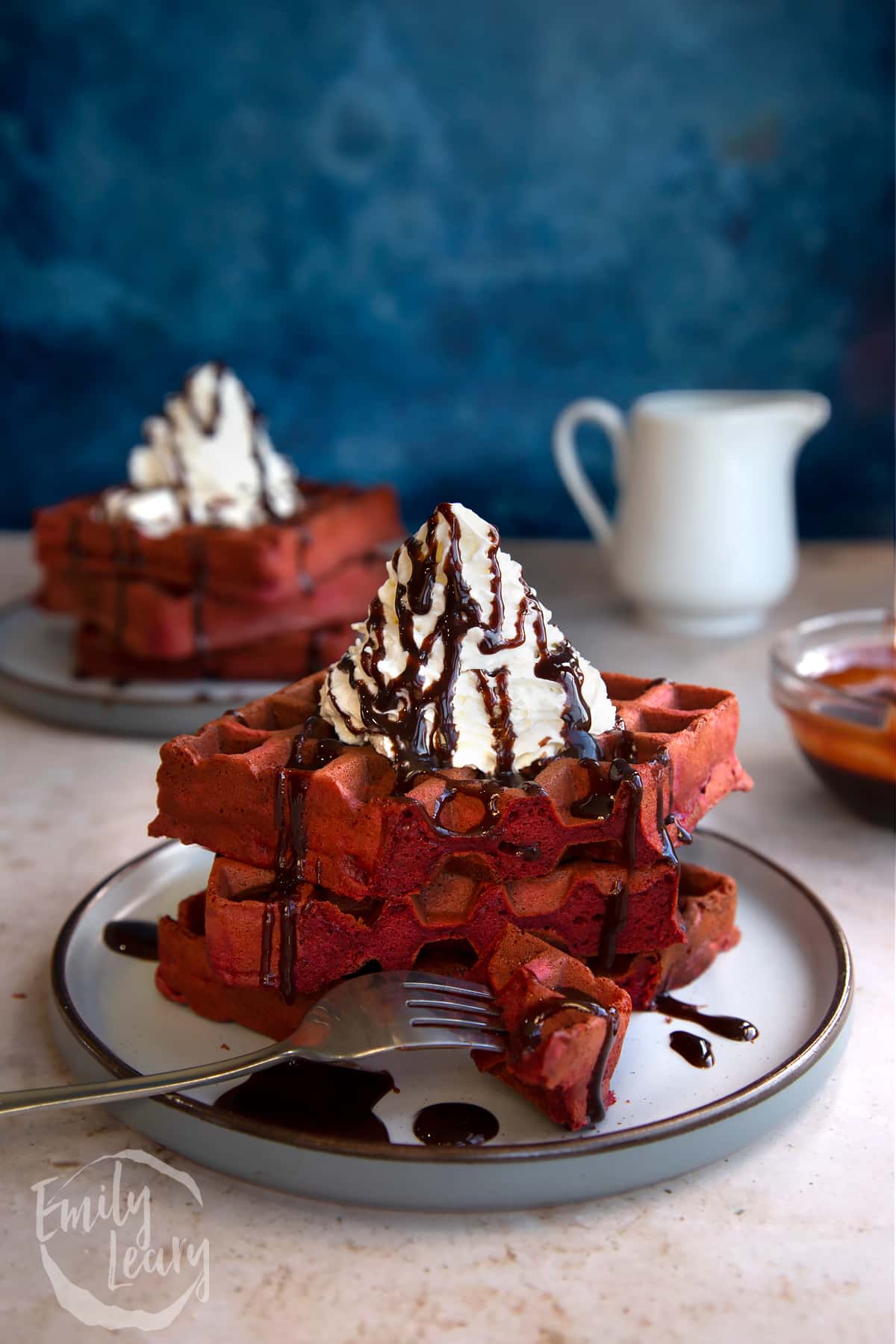 Stack of red velvet waffles topped with whipped cream served on a decoative plate.