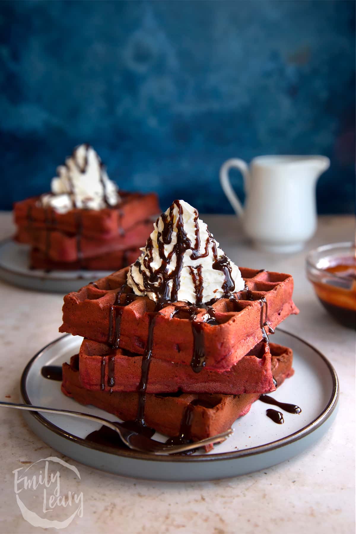 Stacked red velvet waffles topped with whipped cream served on a decoative plate.