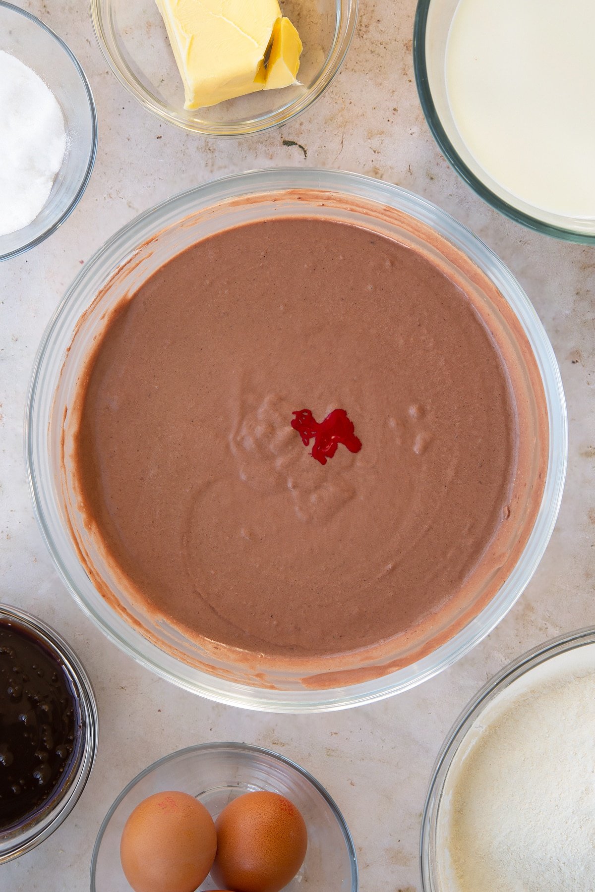 Adding red food colouring to the bowl of red velvet waffle ingredients.