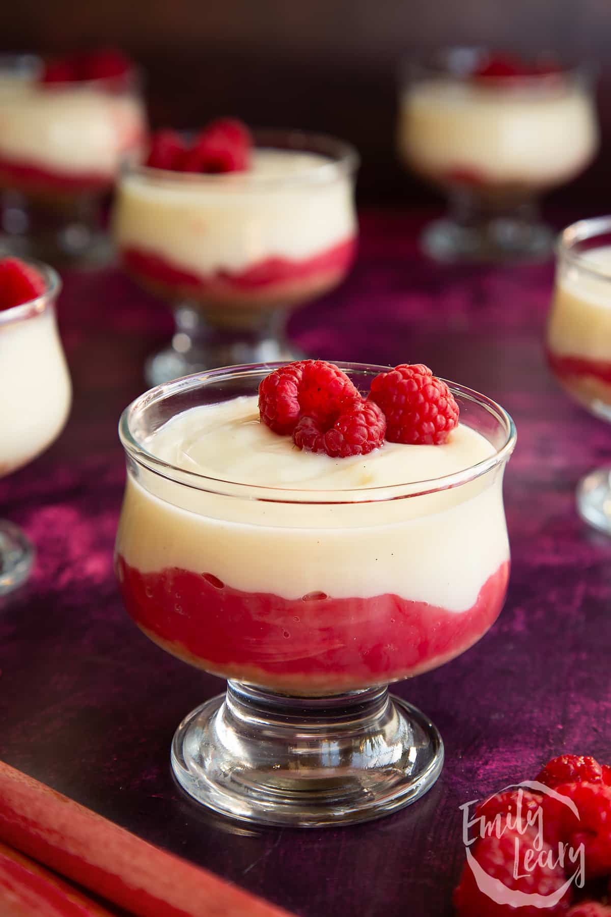 Rhubarb and custard pudding in a glass dish topped with raspberries.