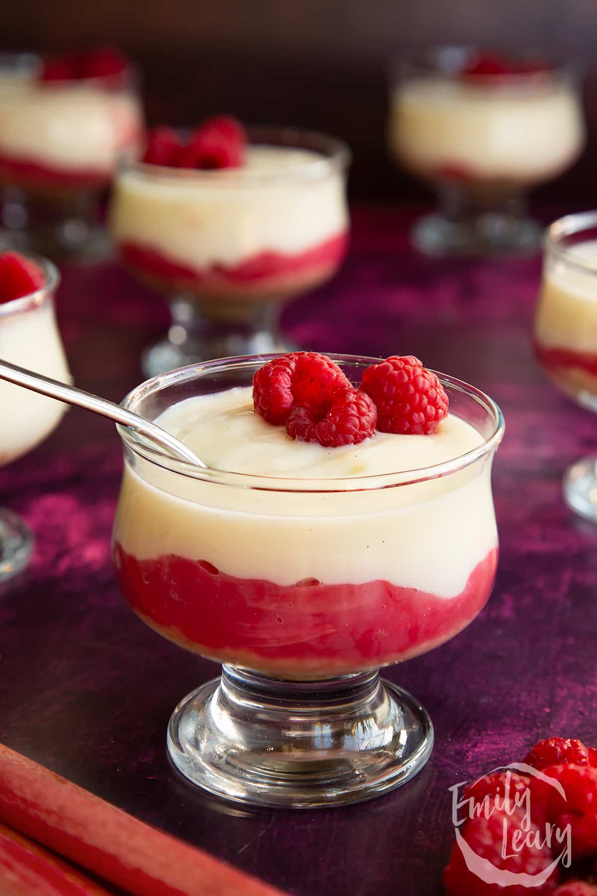 Rhubarb and custard pudding in a glass dish topped with raspberries.