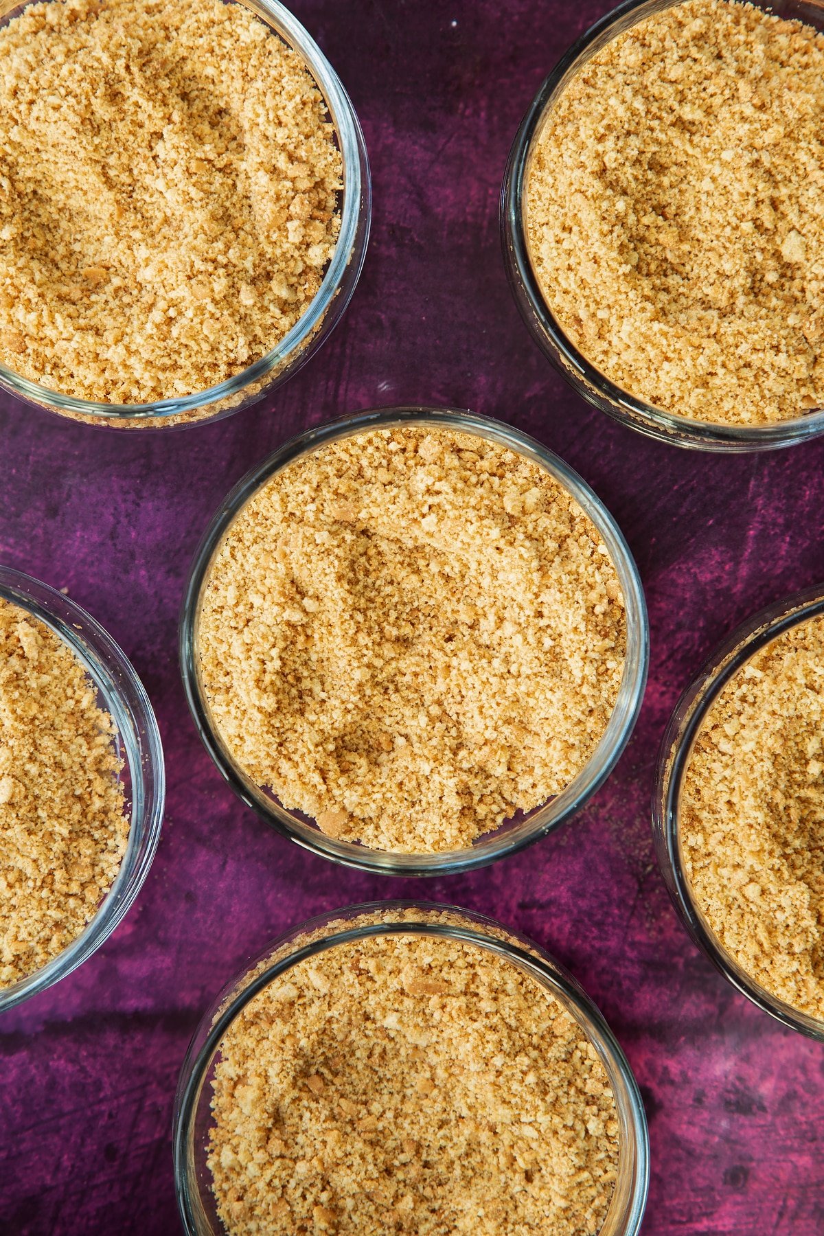 crushed biscuit bases in 6 clear serving bowls on a purple background