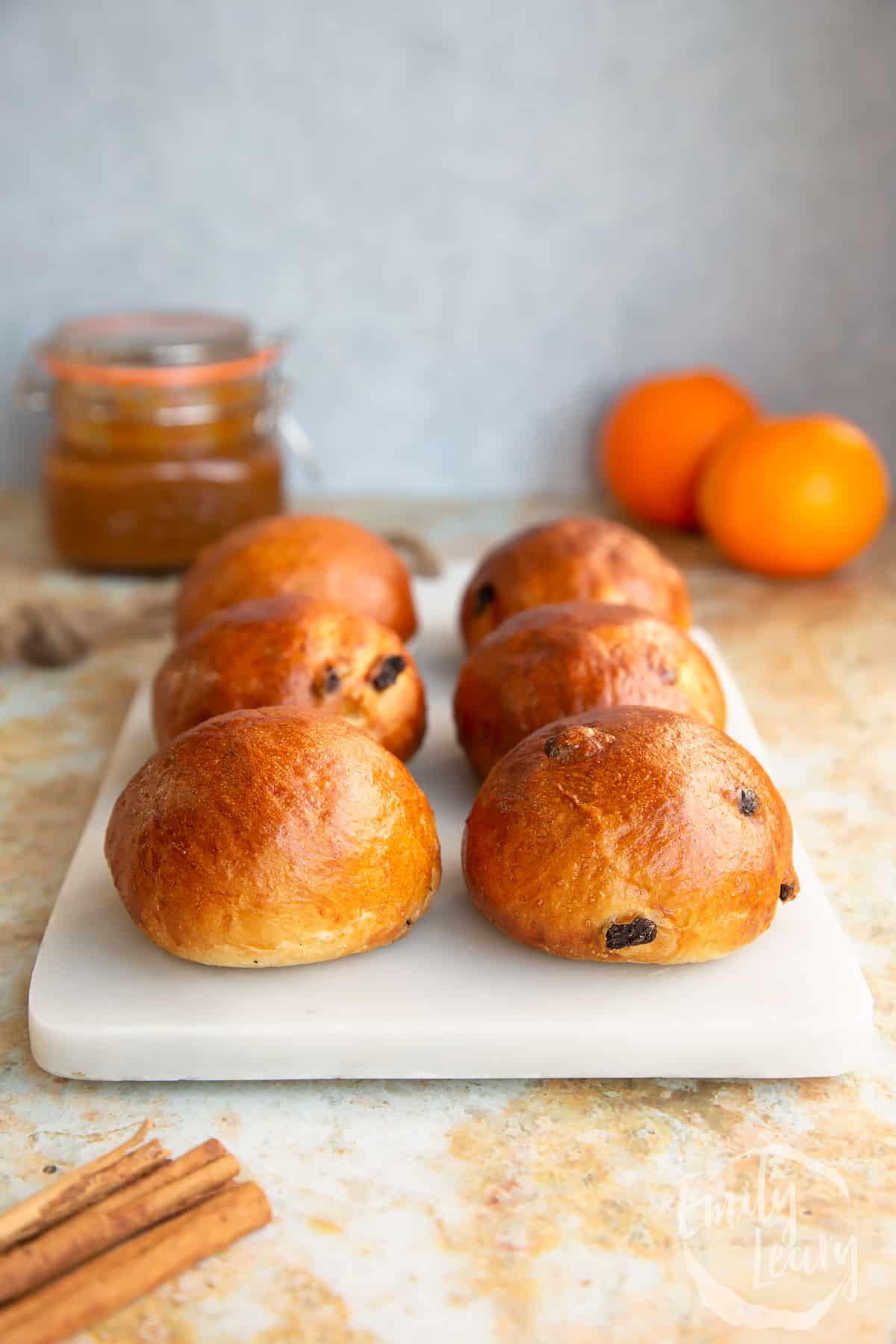 Side on shot of the finished spiced fruit buns on a decoative white board.