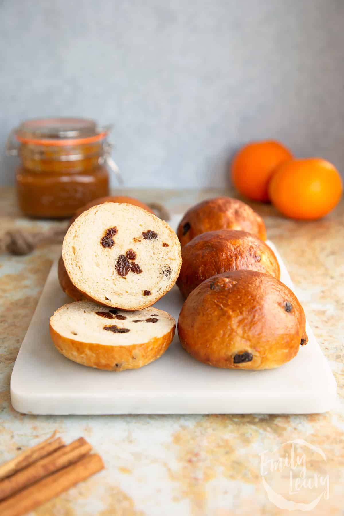 Side on shot of a finished batch of spiced fruit buns sliced in half on a decorative board.