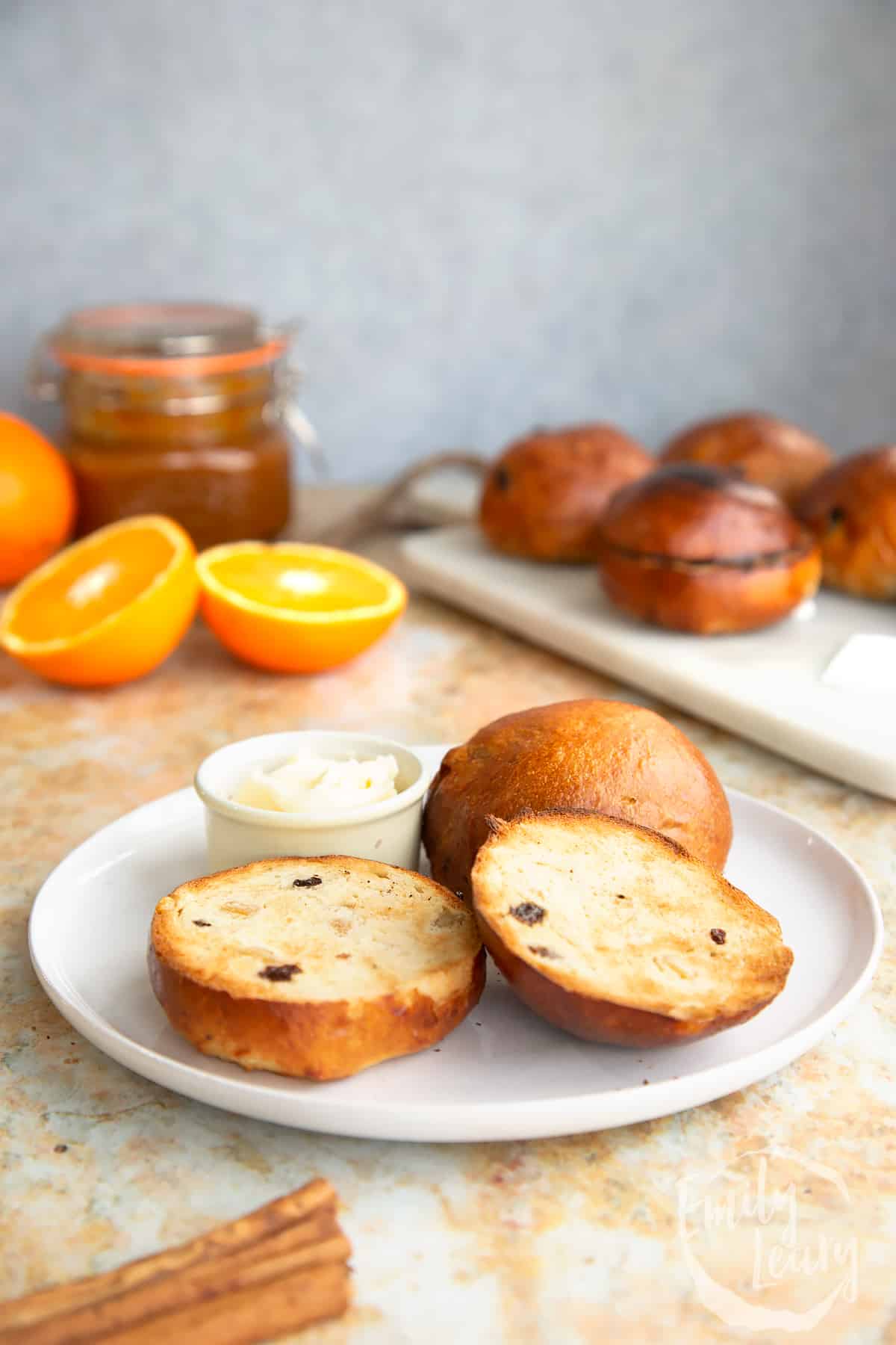 Side on shot of a finished spiced fruit buns sliced open served on a white plate.