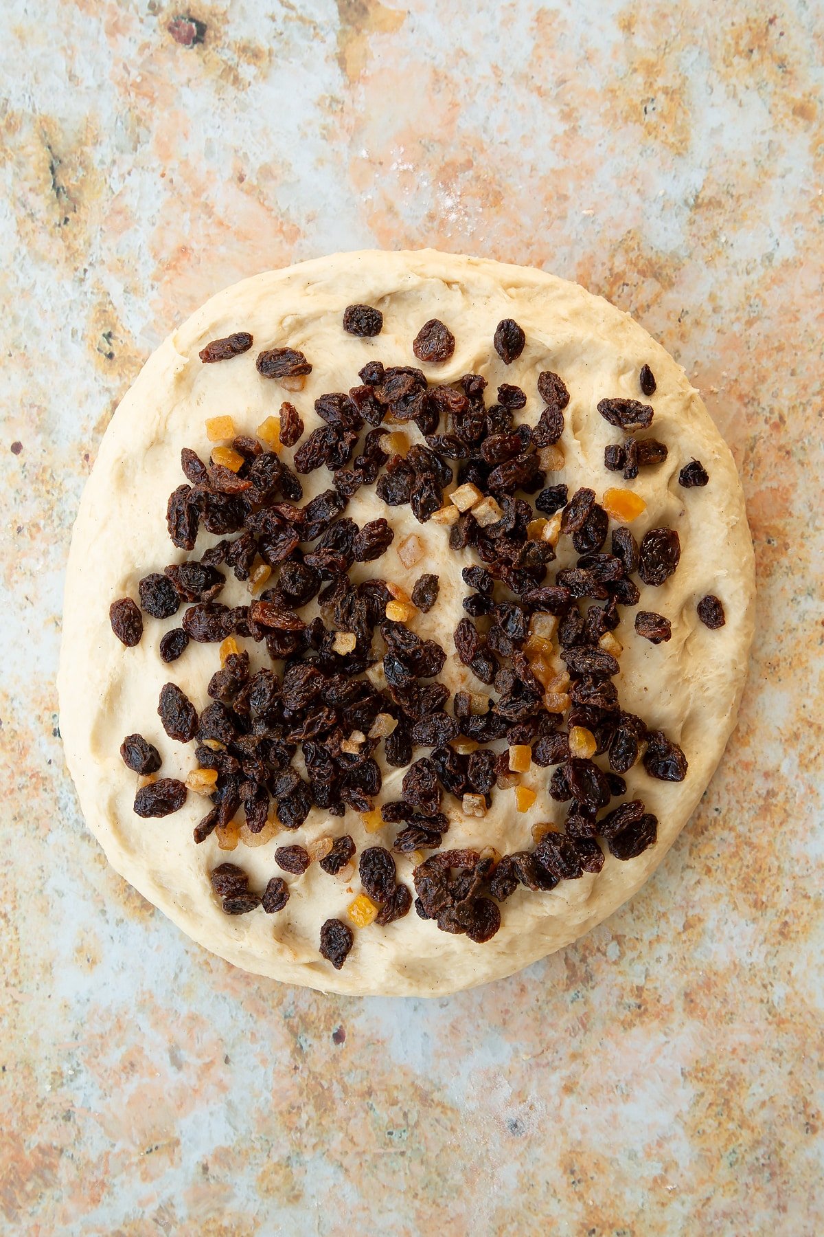 Overhead shot of the mixed fruit being added to the top of the spiced fruit buns dough.