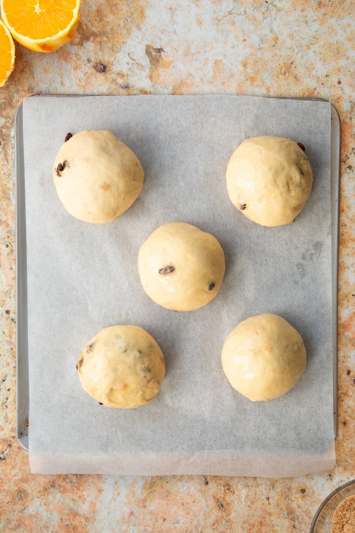 Overhead shot of the balls of spiced fruit buns dough having been baste.