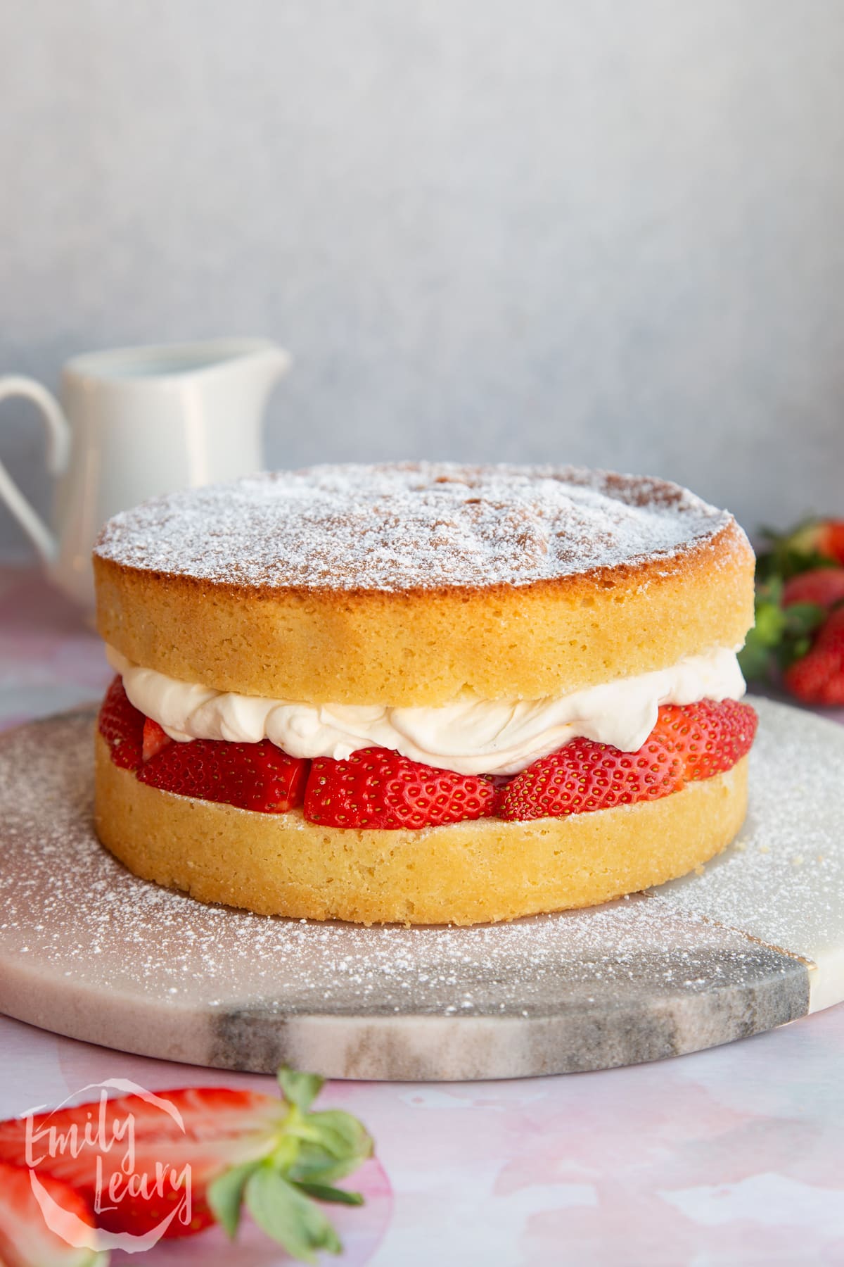 a whole Strawberry cream sponge cake with layers of sponge, cream and strawberries topped with icing sugar