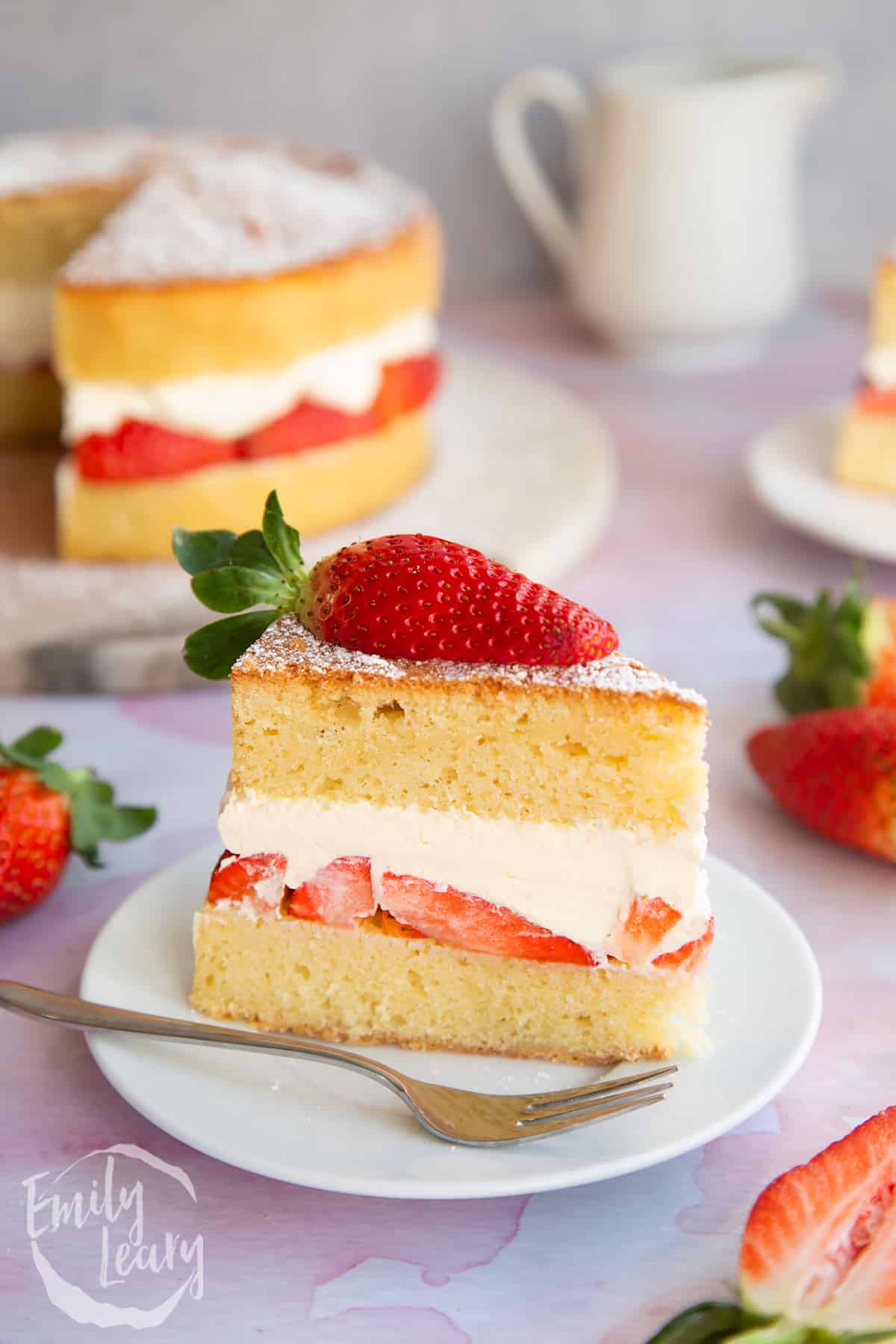 a slice of Strawberry cream cake on a white plate with a small fork with strawberries on top.