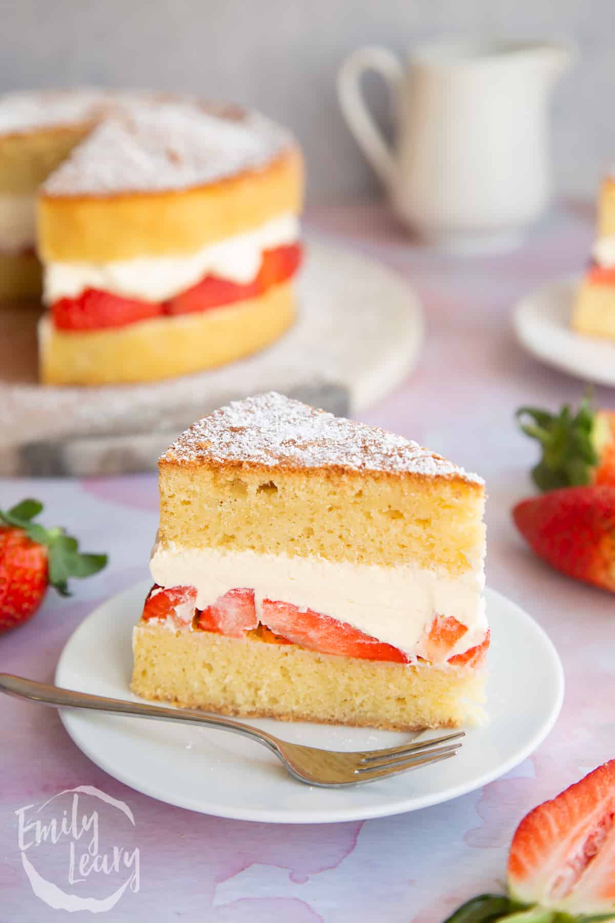 a slice of sponge cake with layers of fresh cut strawberries and fresh cream topped with icing sugar.