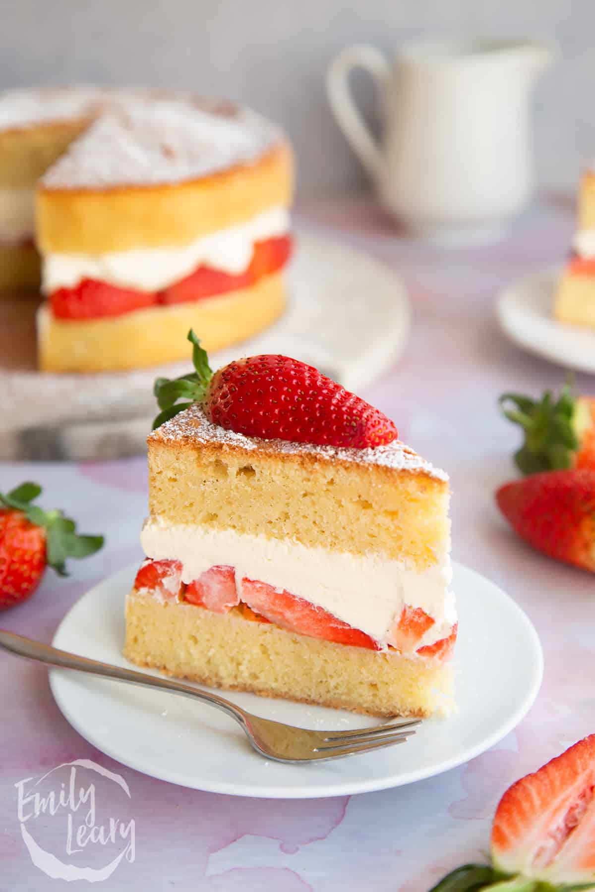 a slice of Strawberry cream cake on a white plate with a small fork with strawberries on top.