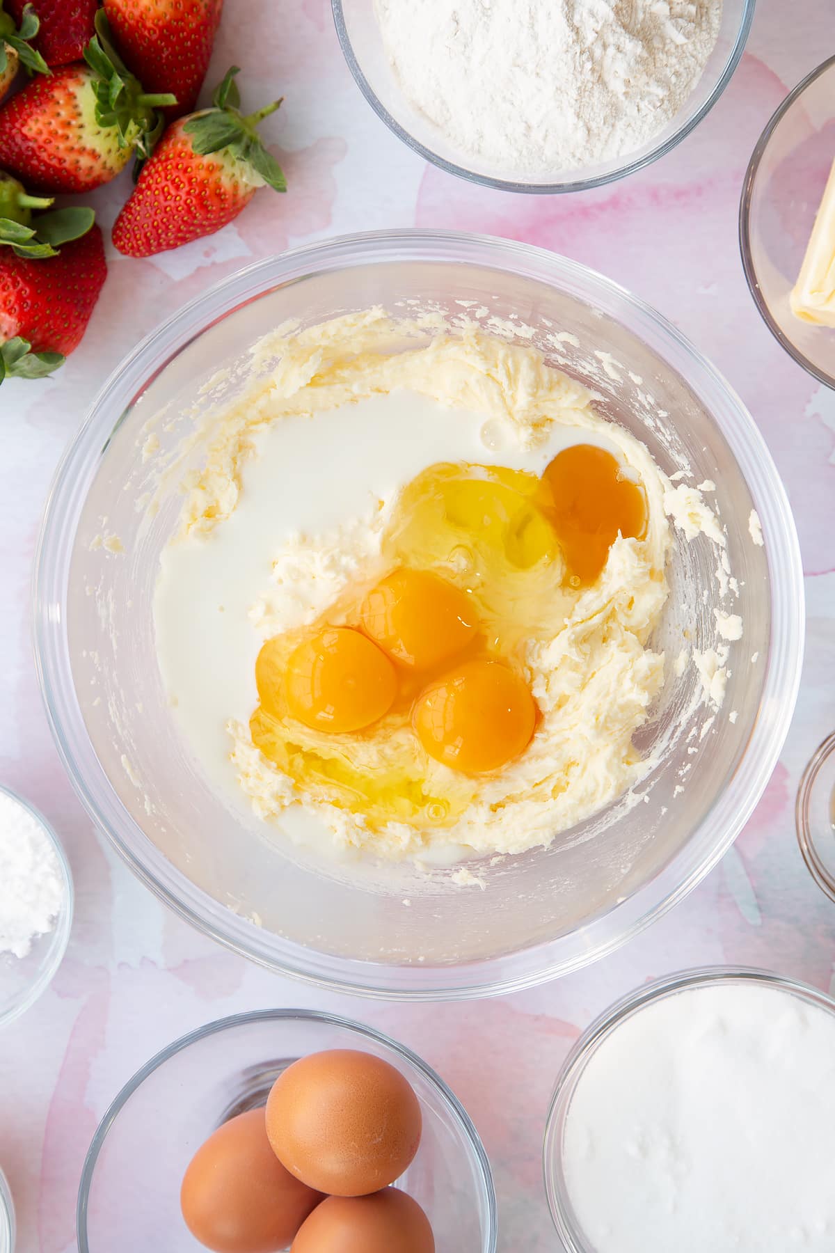 creamed butter and sugar  topped with eggs in a large clear bowl with ingredients around the edges