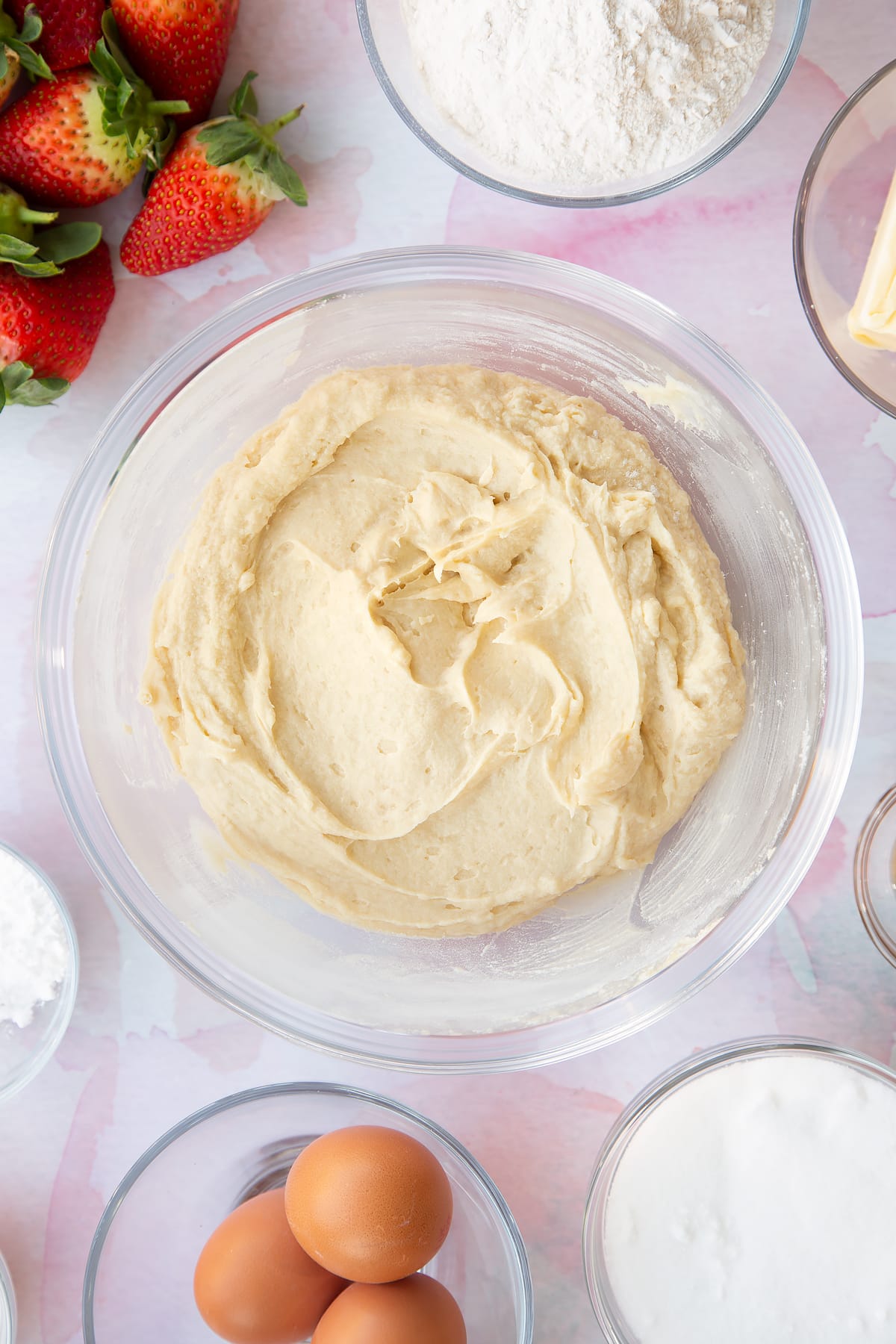 creamed sponge mixture in a large clear bowl with ingredients around the edges