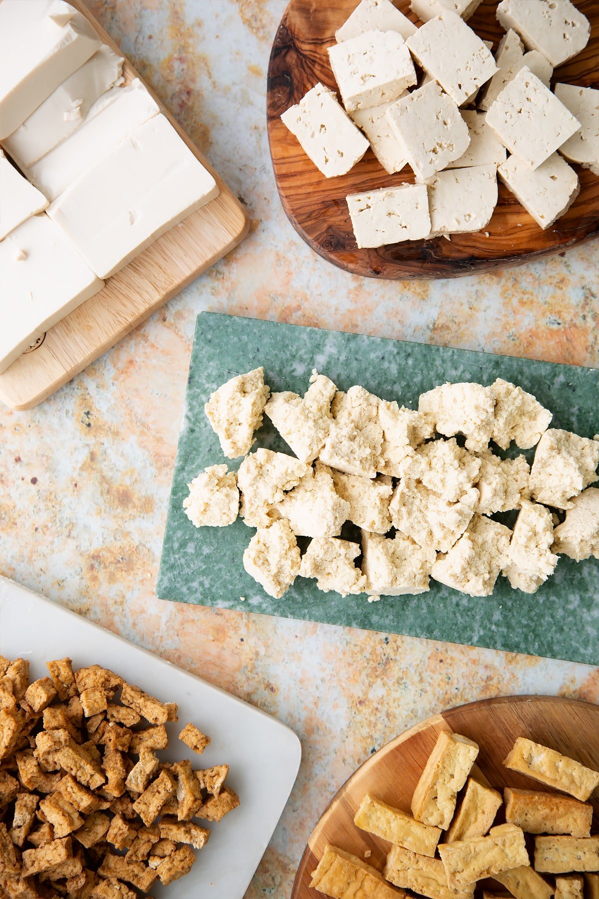 different types of tofu, cut up into strips, cubes and crumbles presented on wooden chopping boards.