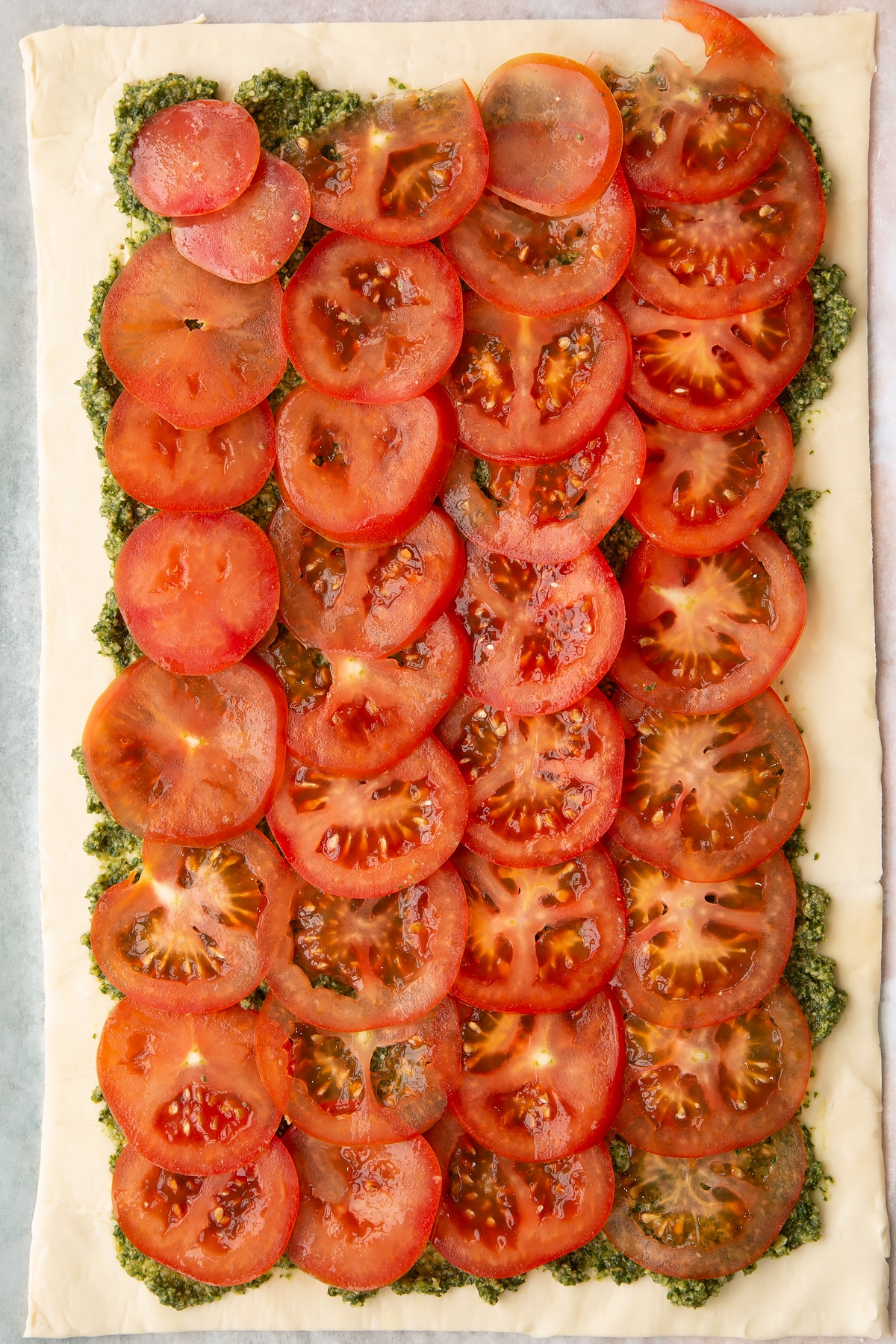 Adding sliced tomatos ontop of the puff pastry covered in pesto.