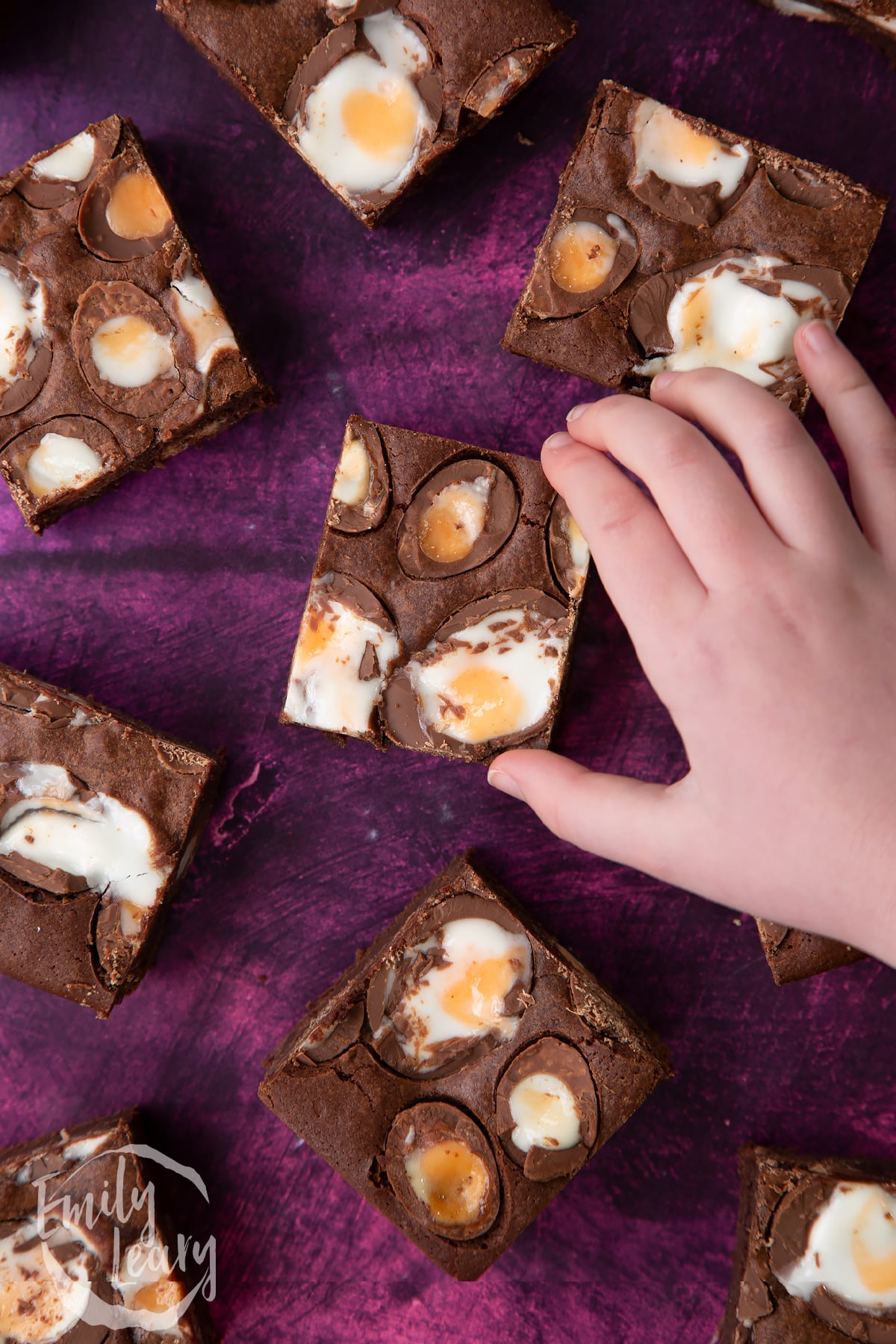Hand reaching in to grab a finished Cadbury Creme Egg brownie.