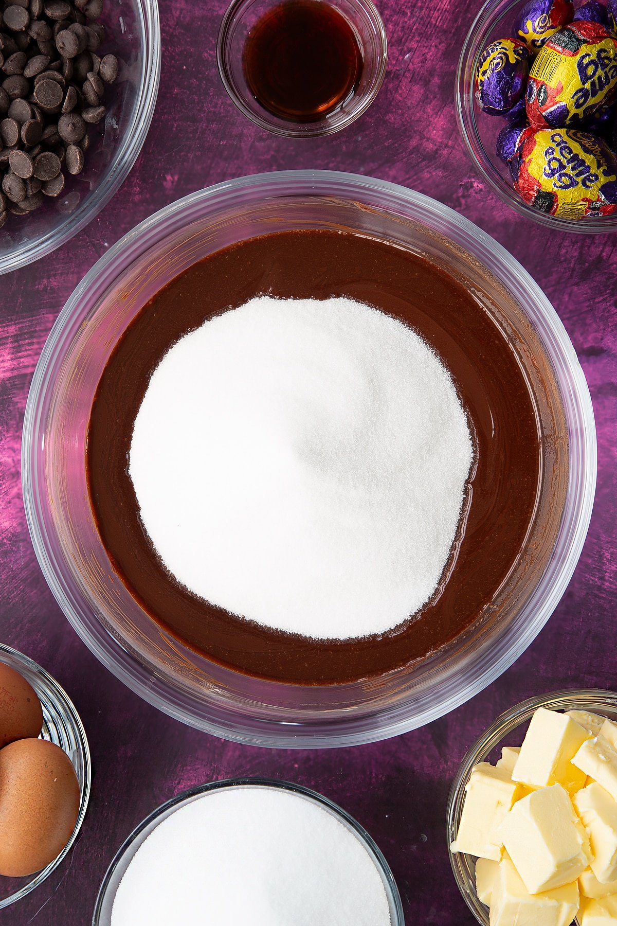 Adding sugar to the butter and chopped dark chocolate in a large, heatproof bowl