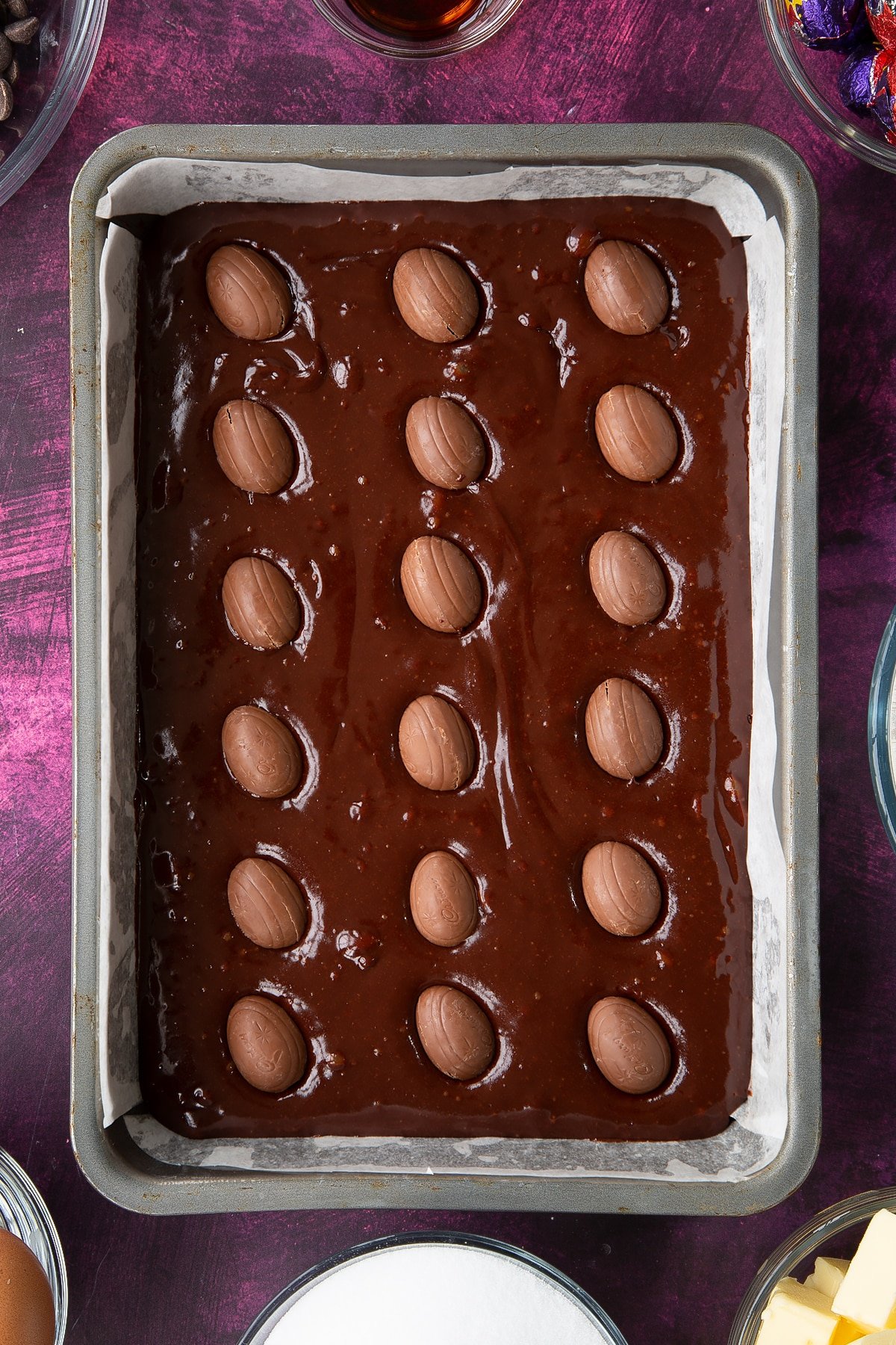 Overhead shot of a baking tin lined with paper and the chocolate mixture and cadburys mini eggs inside. 