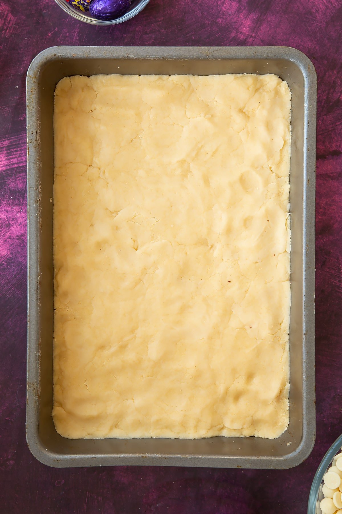 Spreading the mixture evenly across the rectangular baking tin and pressing it down firmly.