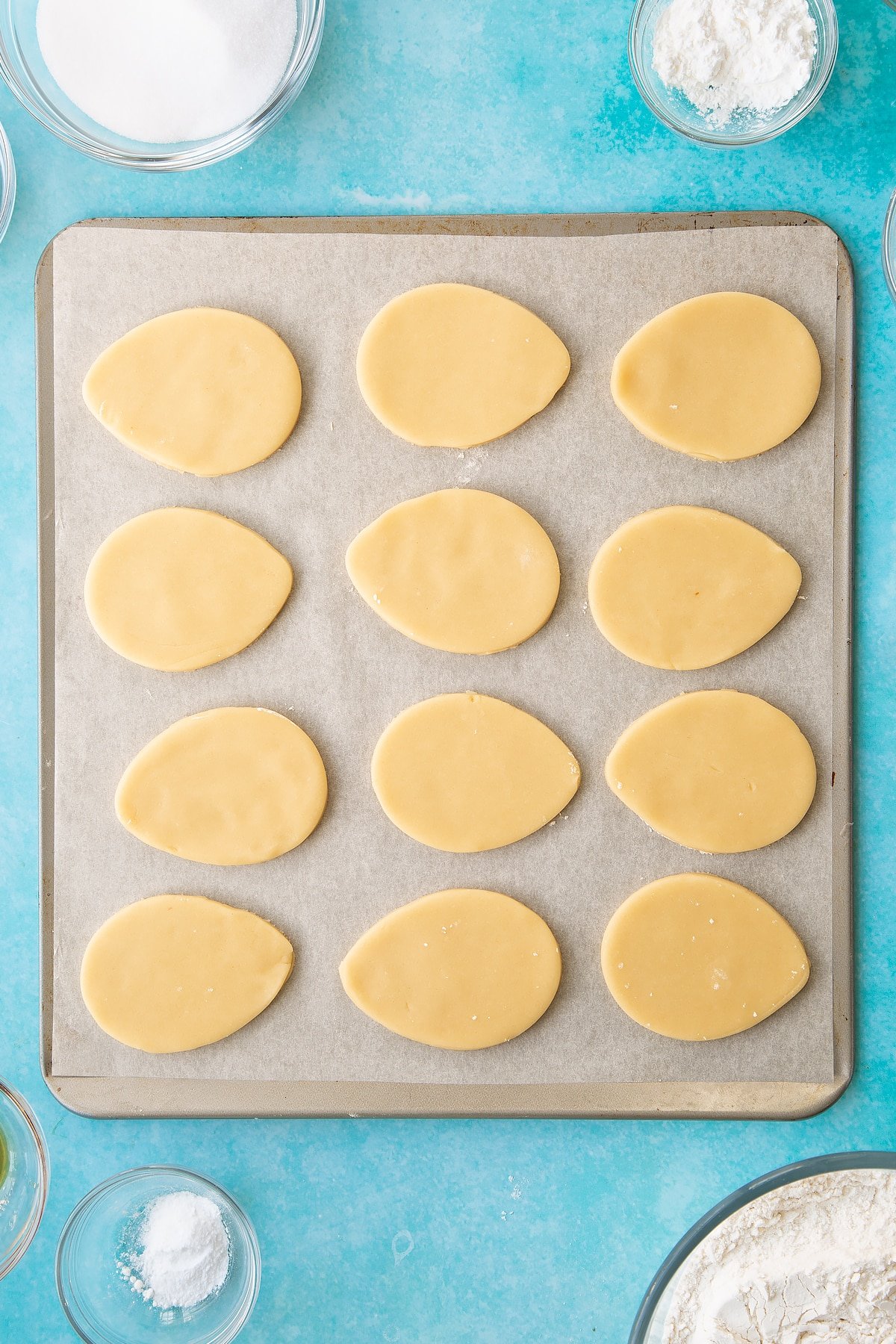 Overhead shot of the cookie dough having had egg shapes cut out of it using the cookie cutter. 