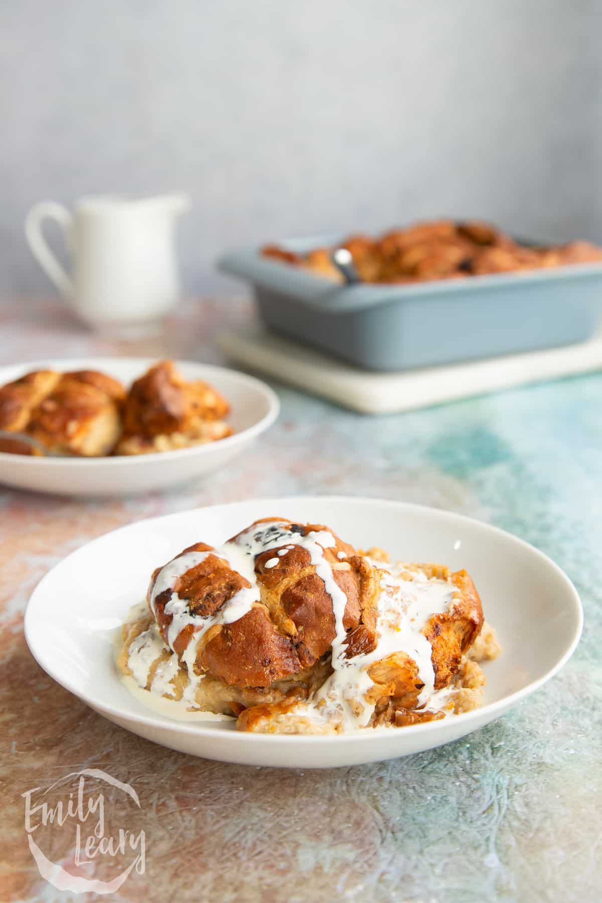 Side on shot of the finished hot cross bun bread and butter pudding in a bowl topped with cold cream.