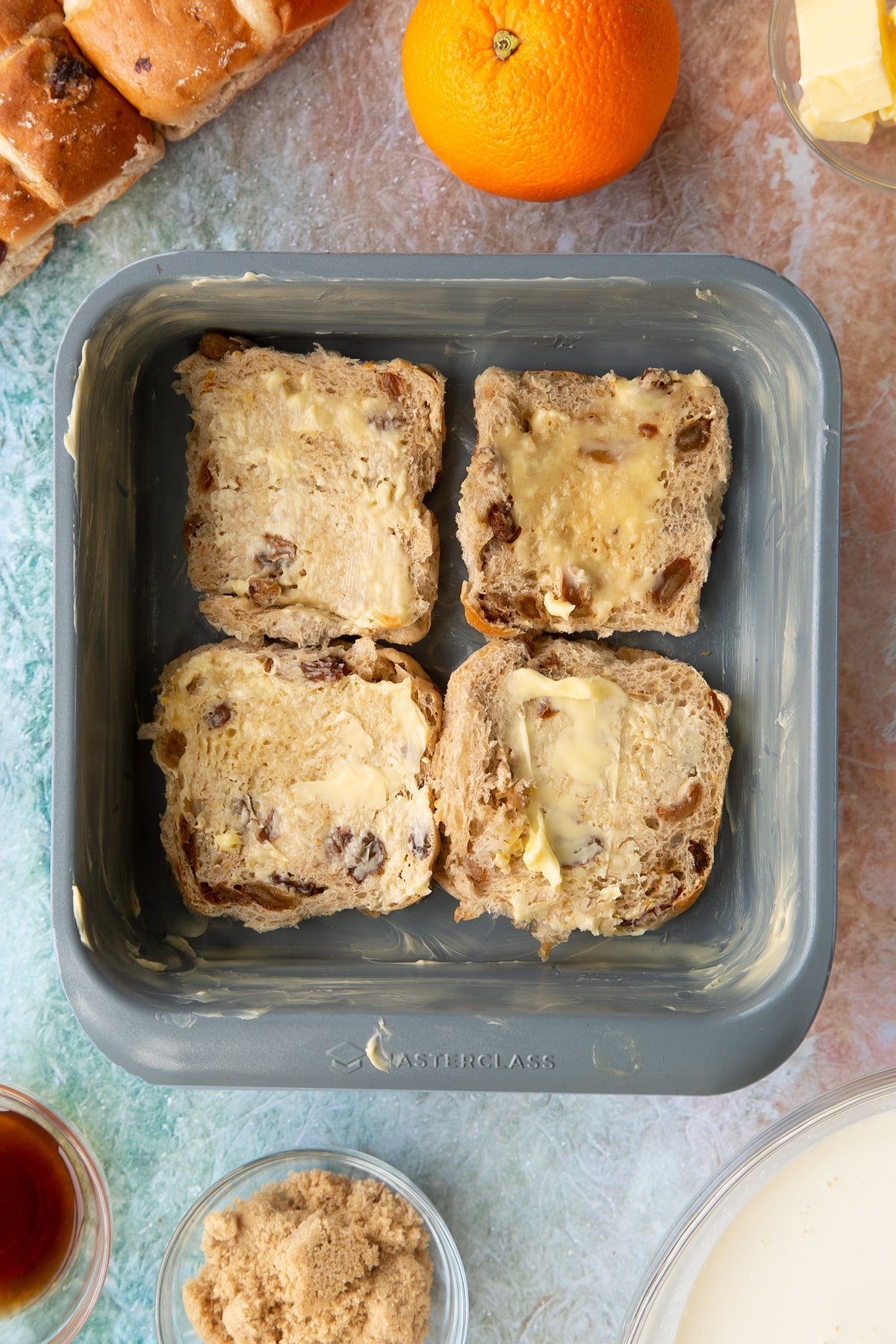 A tin with the bottom of the sliced hot cross buns inside coated in butter. 