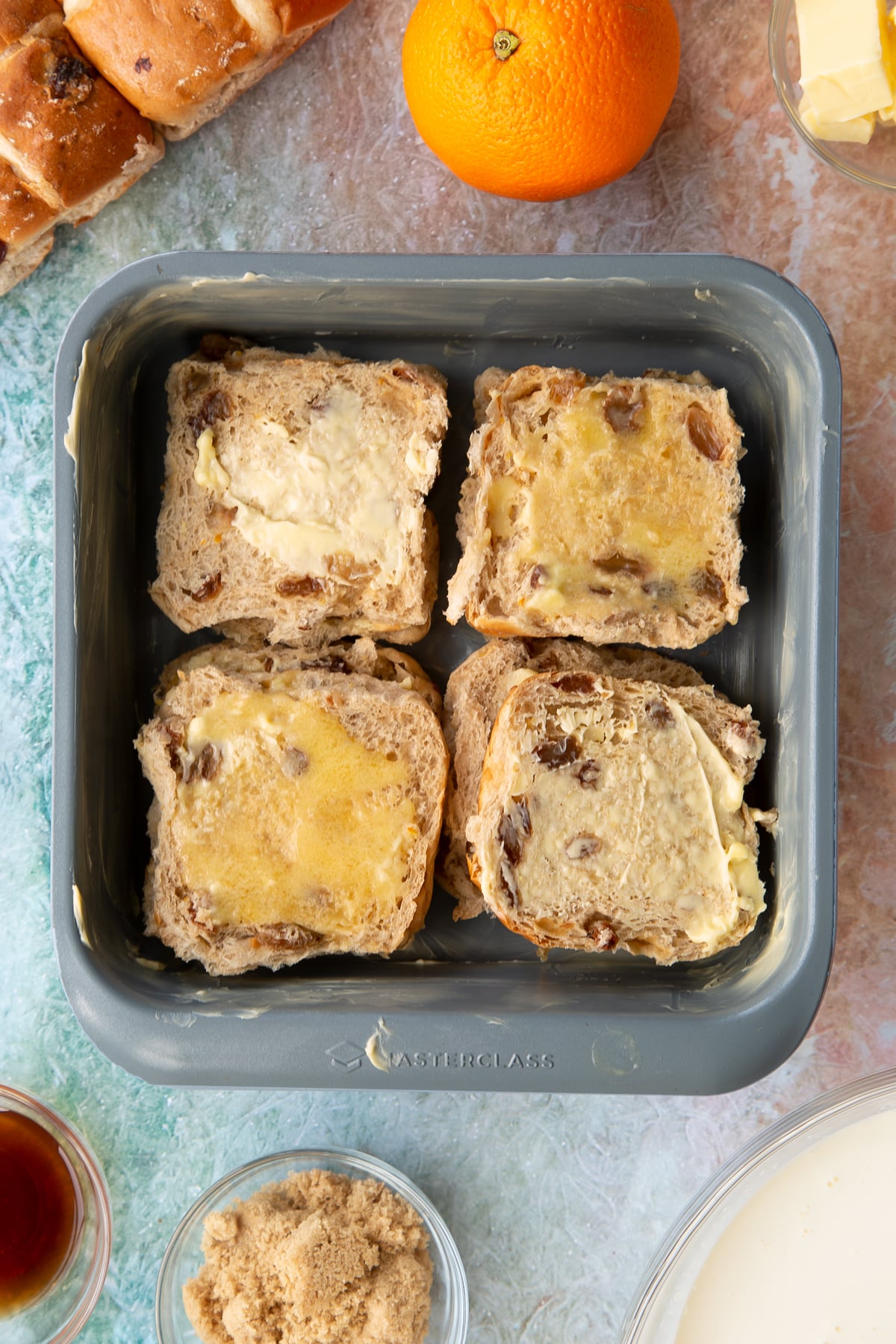 A tin with the bottom of the sliced hot cross buns inside coated in butter. 