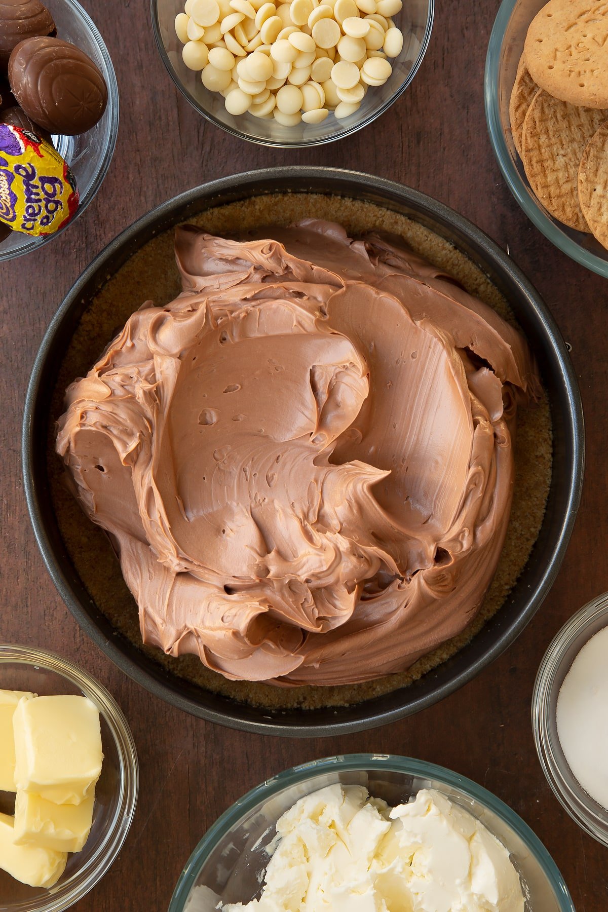 Overhead shot of the Cadbury Creme Egg cheesecake filling being added to the top of the crumbled biscuit base in a loose-bottom cake tin.