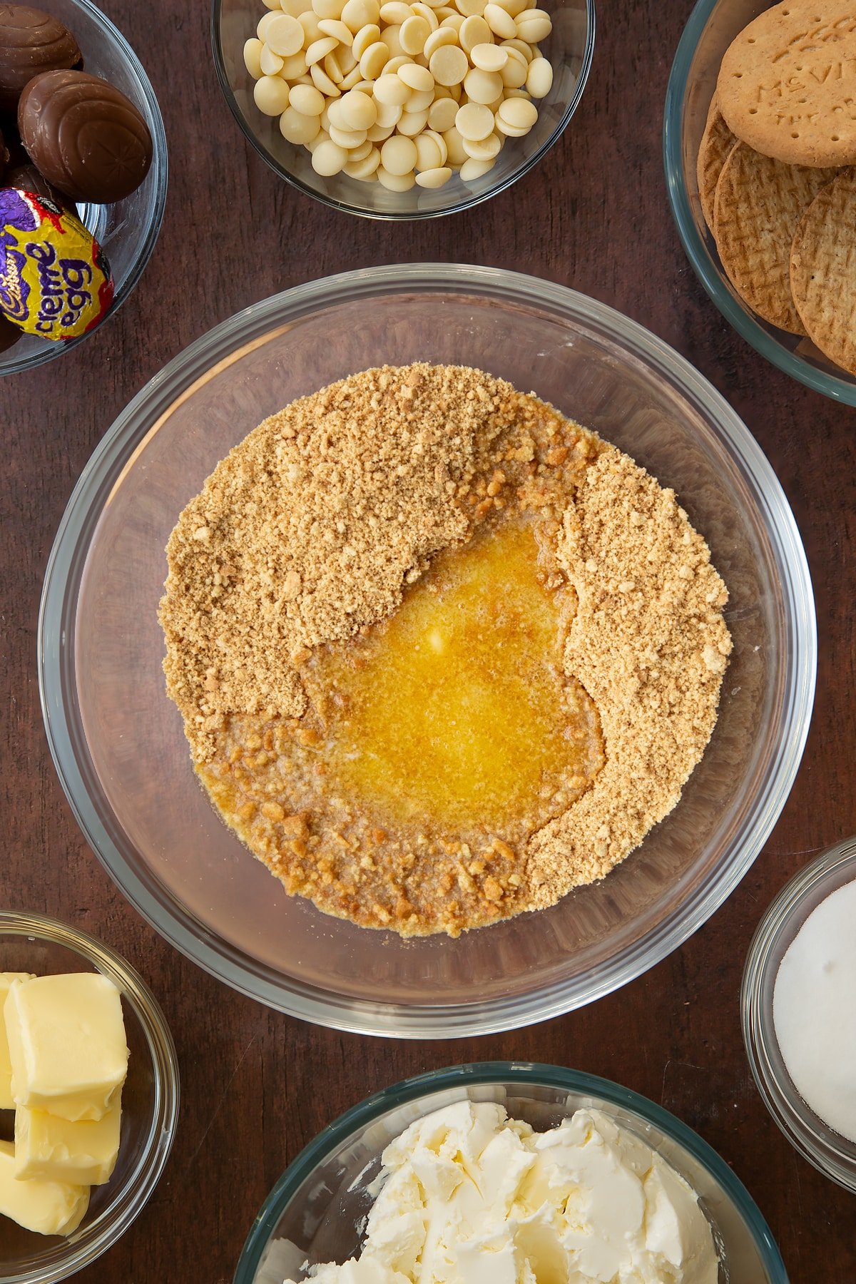 Adding butter to the bowl of crumbled biscuits. 