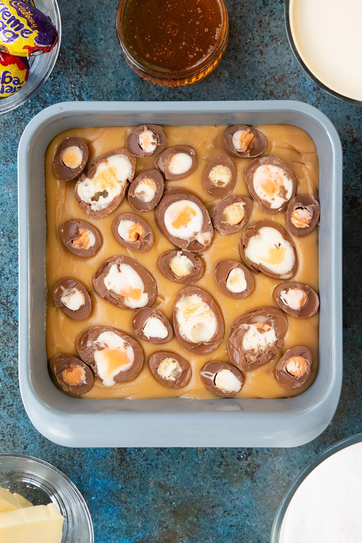 Adding sliced creme eggs onto the top layer of the fudge inside a baking tray.