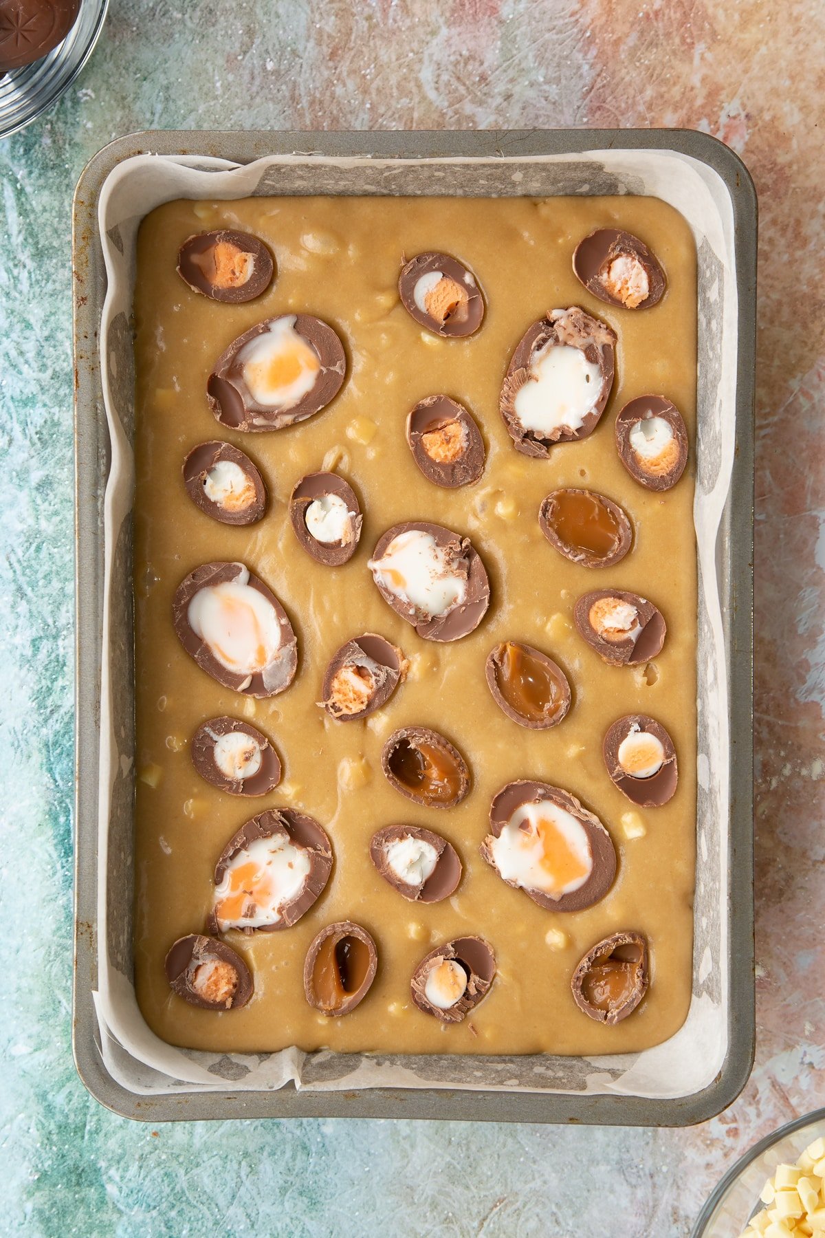 Overhead shot of sliced creme eggs being added to the wet easter blondies mixture inside a baking tin.