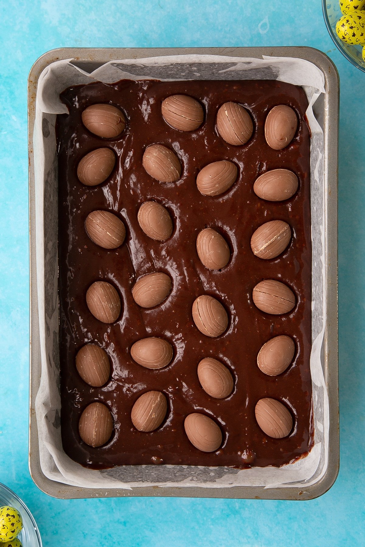 Adding the creme eggs to the lined rectangular cake tin with the easter brownies wet mixture inside.