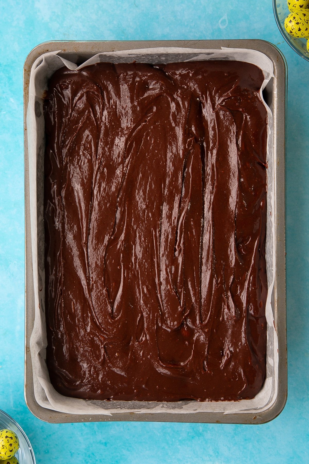 Folding in the second layer of the easter brownies wet mixture ontop of the creme eggs.