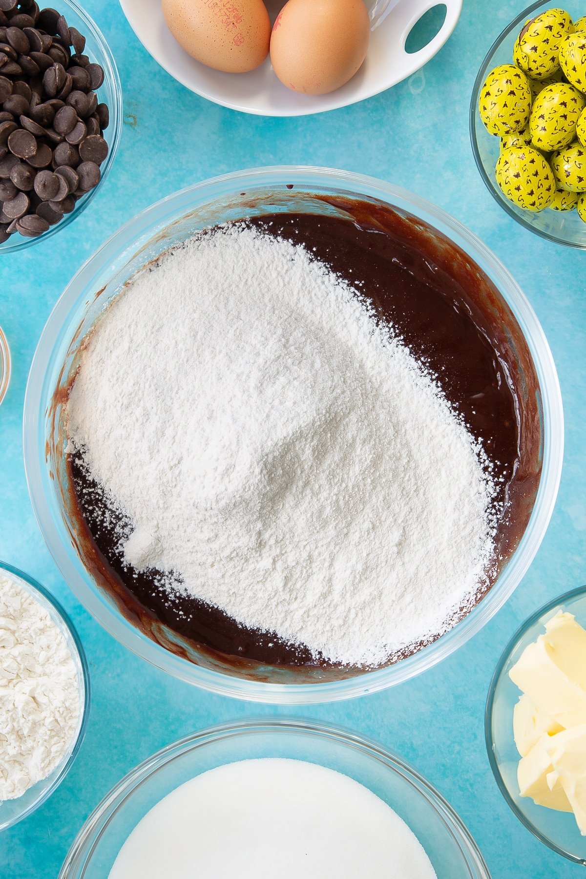 Overhead shot of sieved flour being added to the wet easter brownies mixture in a mixing bowl.