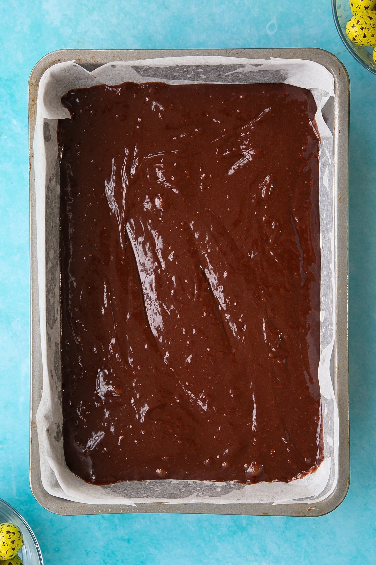 A greased and lined rectangular cake tin with the wet easter brownies mixture inside.